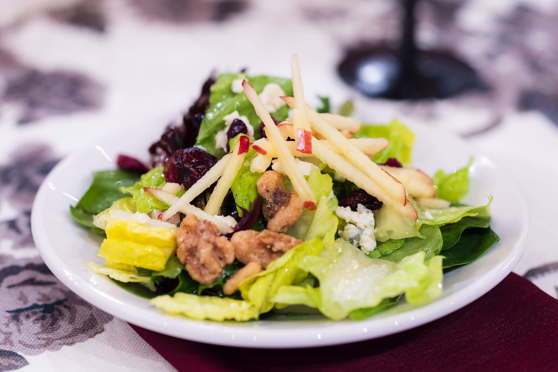 Small plate of mixed salad with greens, apple slices, walnuts, and shredded cheese on a table