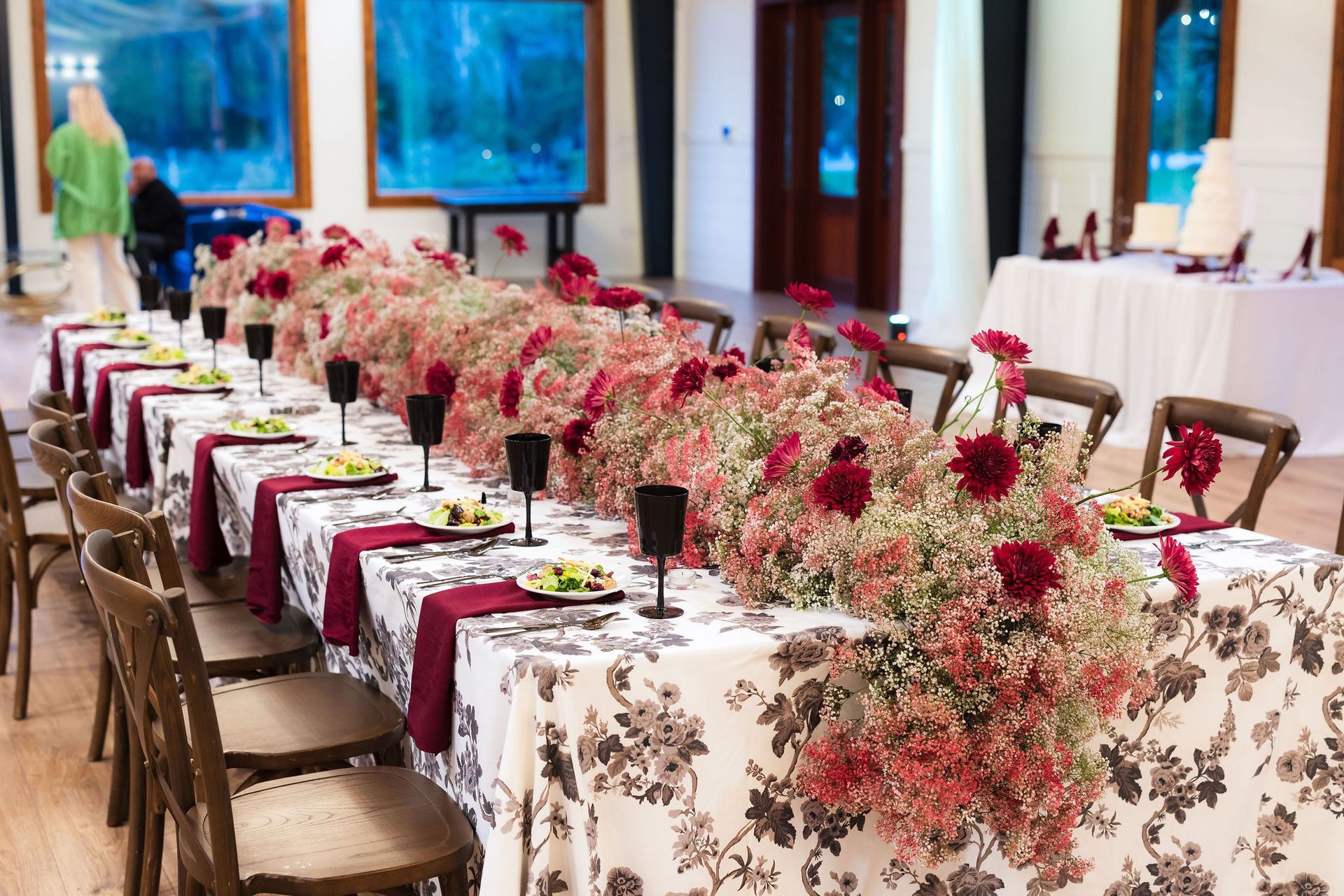 Long banquet tables with floral tablecloths and pink flower centerpieces in a bright dining room
