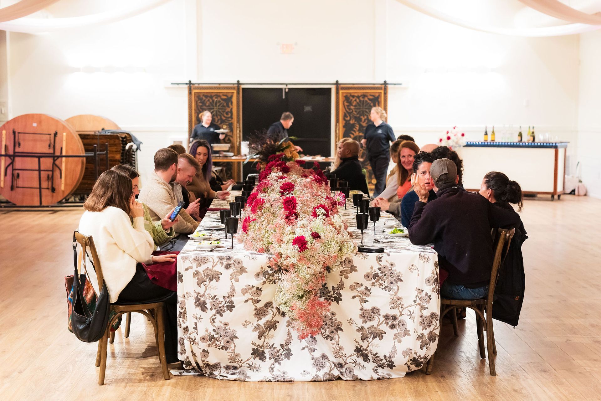 People seated around a flower-covered dining table in a bright room with paintings on the wall