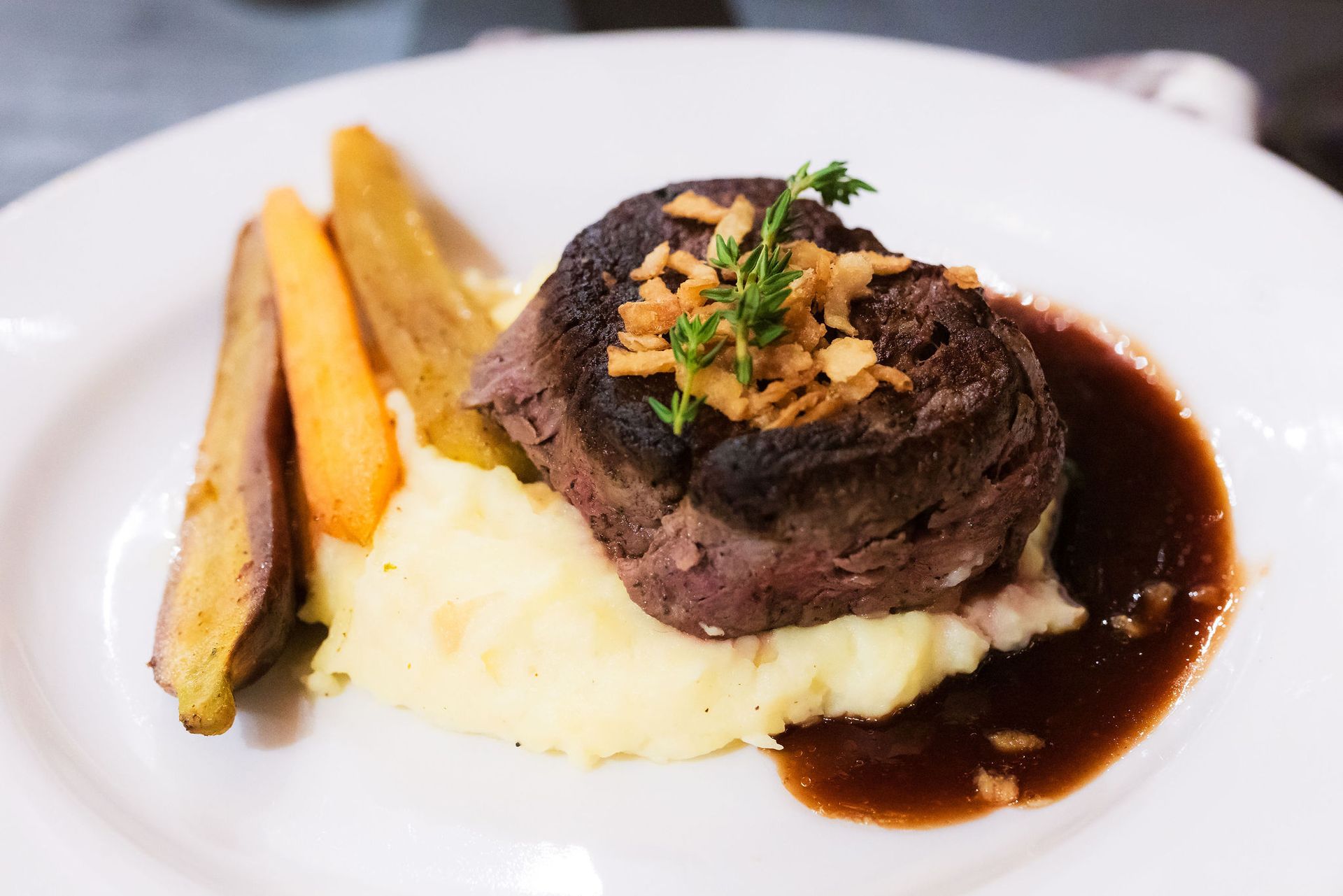 Plated beef medallion with mashed potatoes, carrots, and dark sauce on a white plate