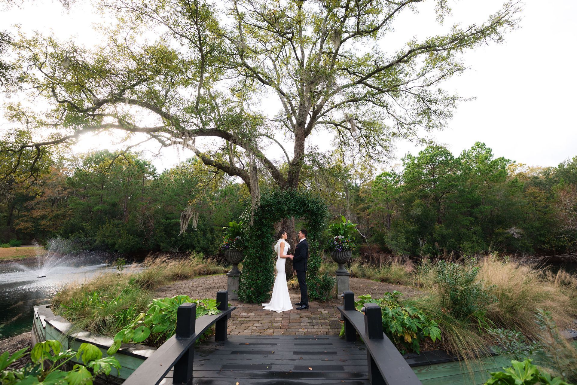 Bride and groom on a wooden bridge in a lush garden with a large tree overhead