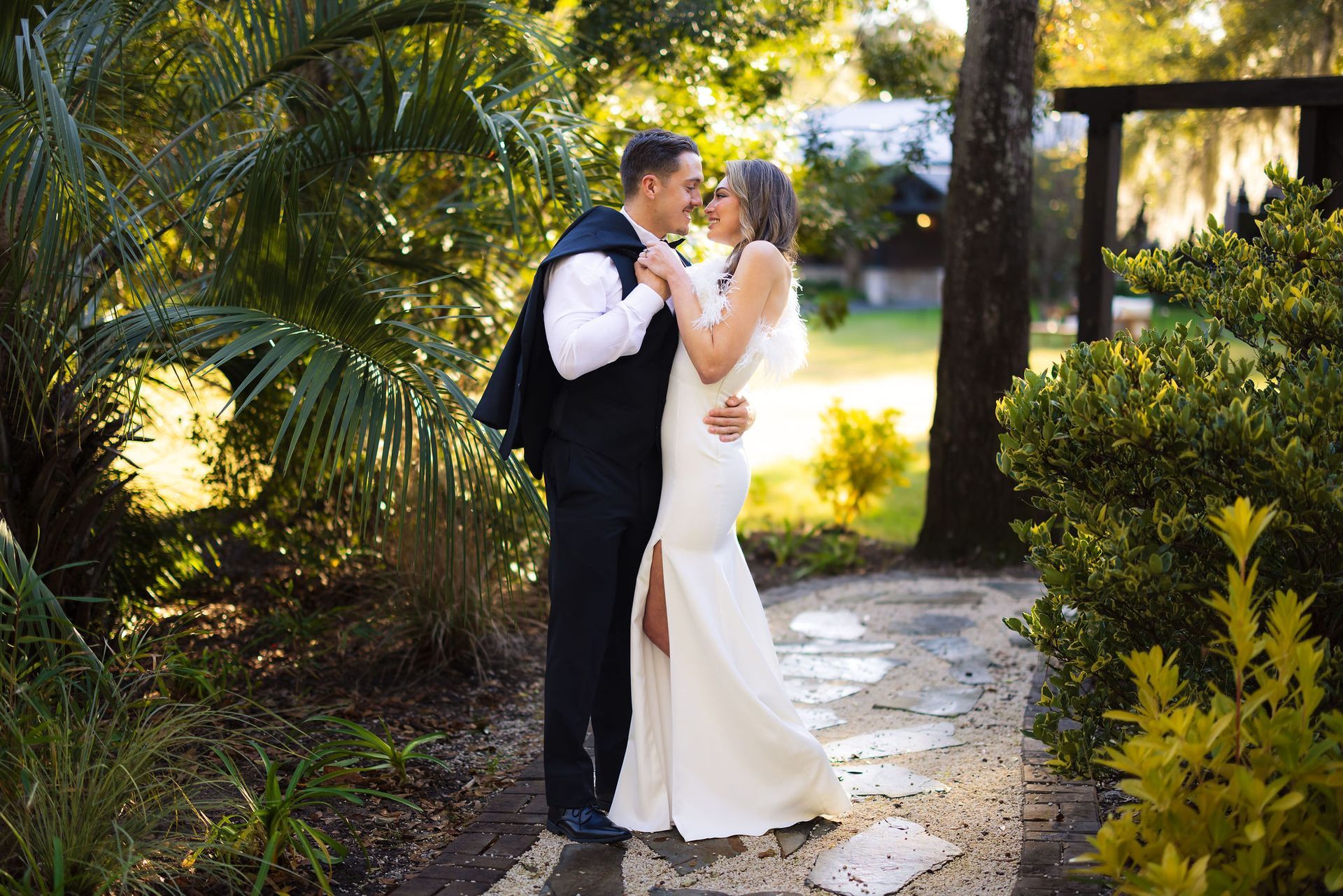 Wedding couple kissing on a garden path, with sunlight and greenery surrounding them