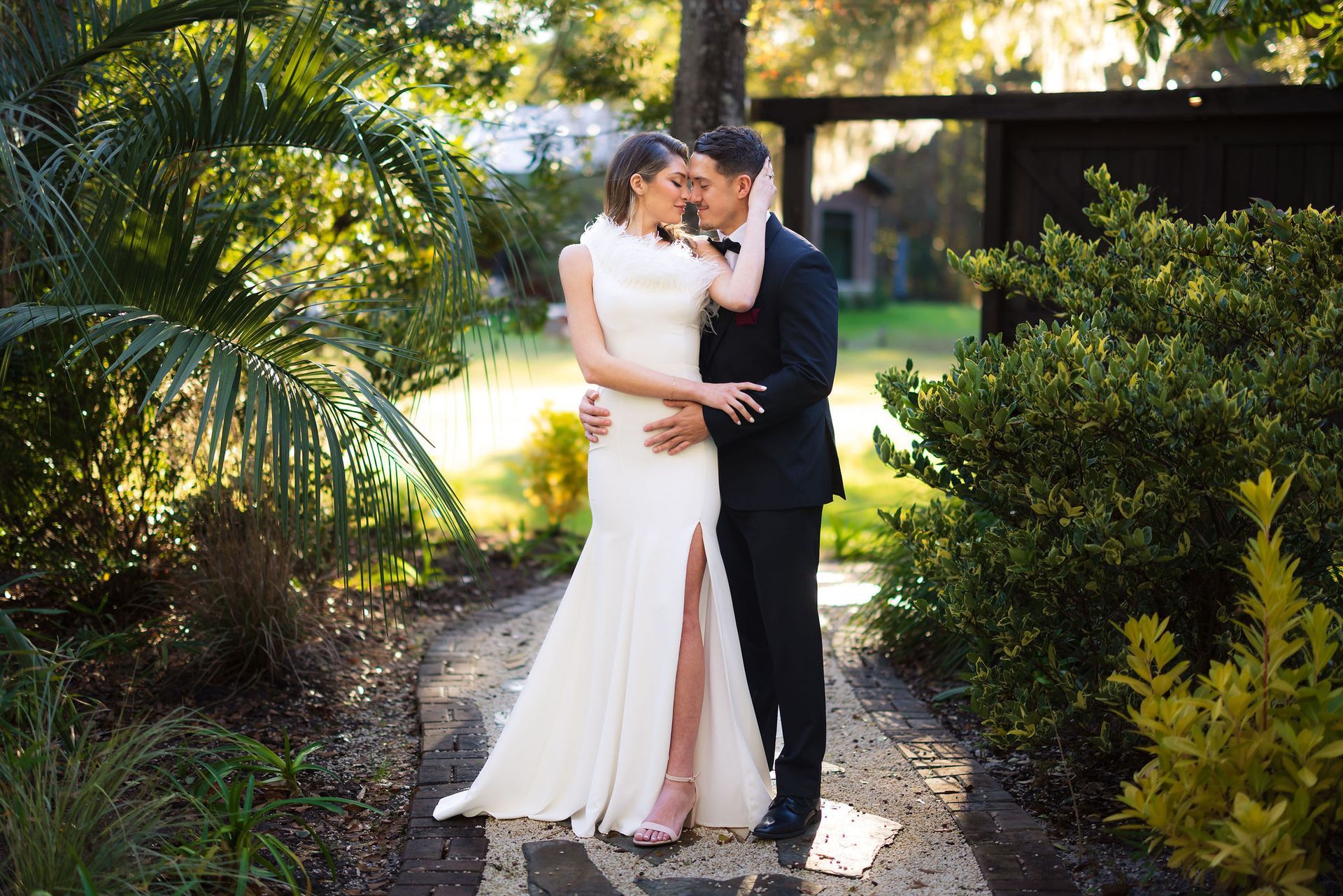Couple in wedding attire embracing in a sunlit garden path