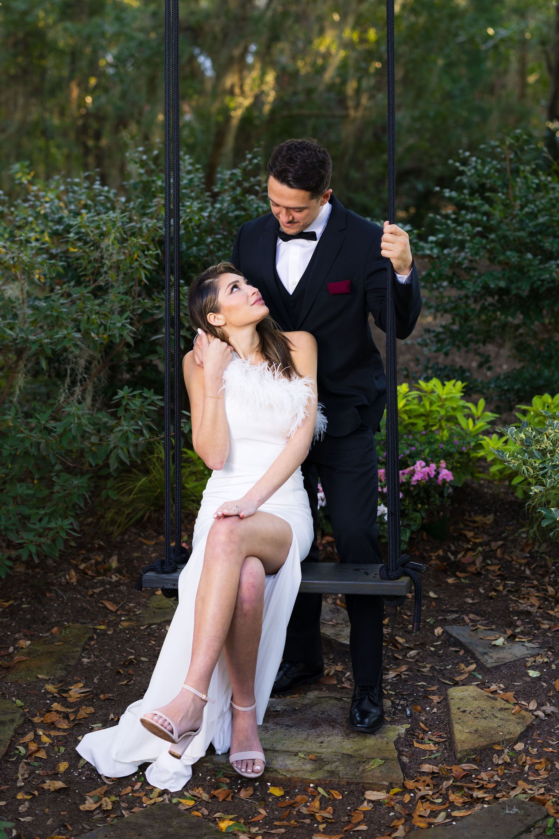 Couple in wedding attire seated on a garden swing, sharing a romantic moment outdoors.