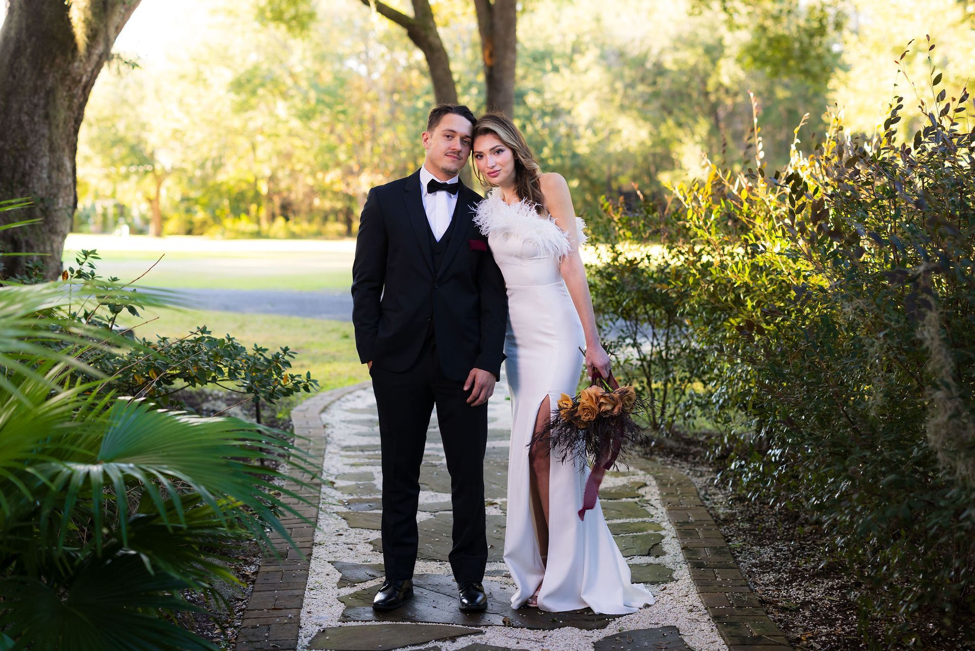 Bride and groom in formalwear standing together on a garden path outdoors