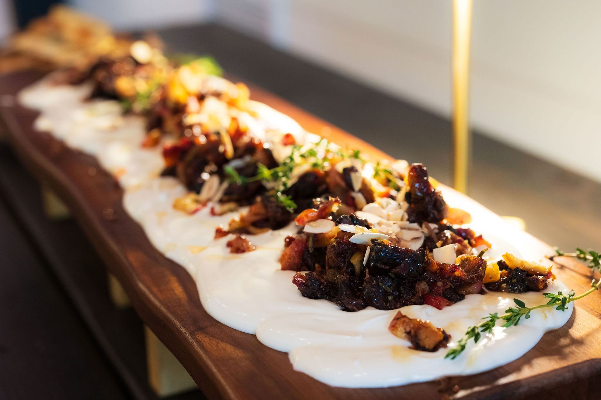 Long rectangular appetizer with white sauce, herbs, and colorful toppings on a wooden board