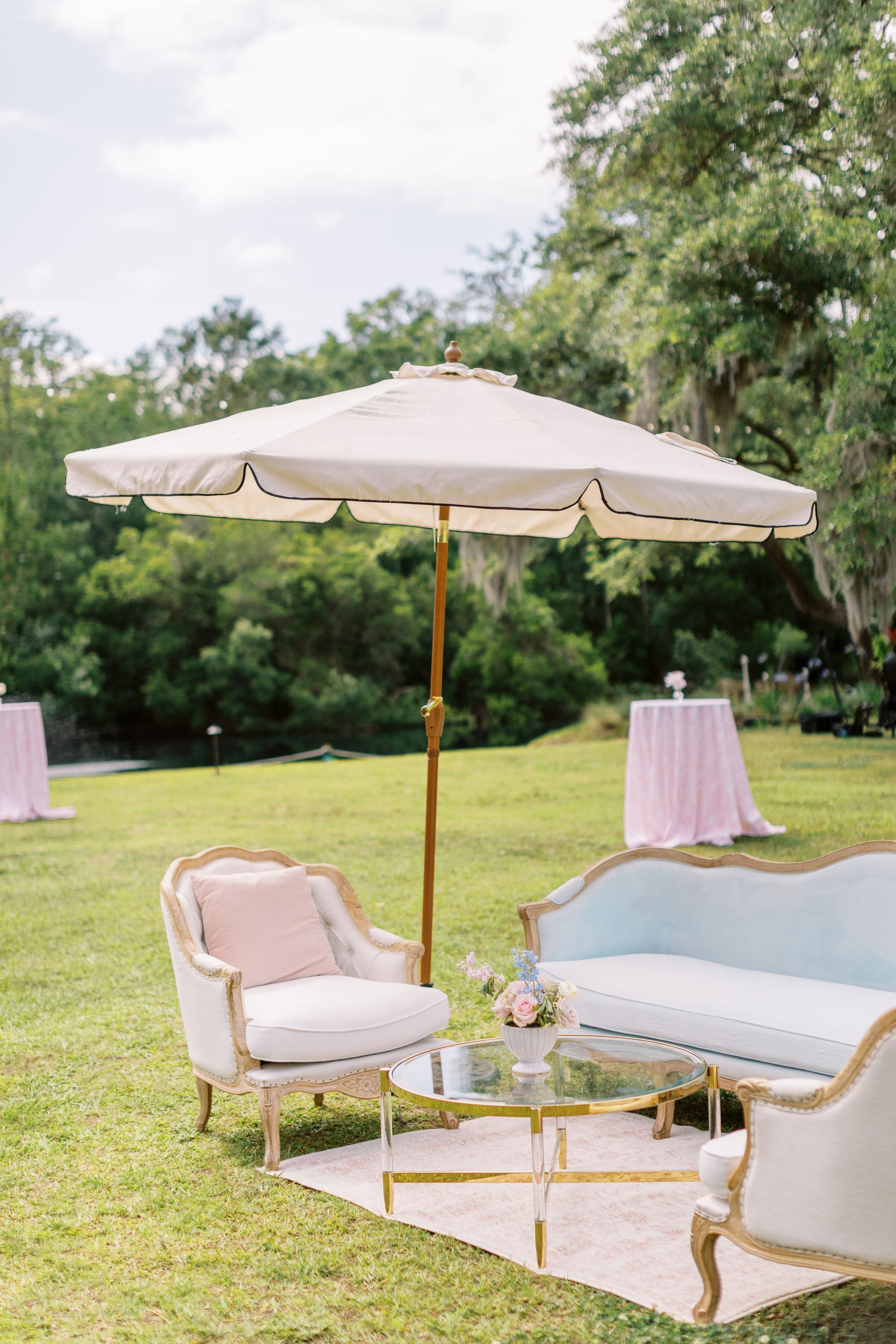 White patio umbrella and pale blue outdoor sofa with matching chair on a lawn for a garden party.