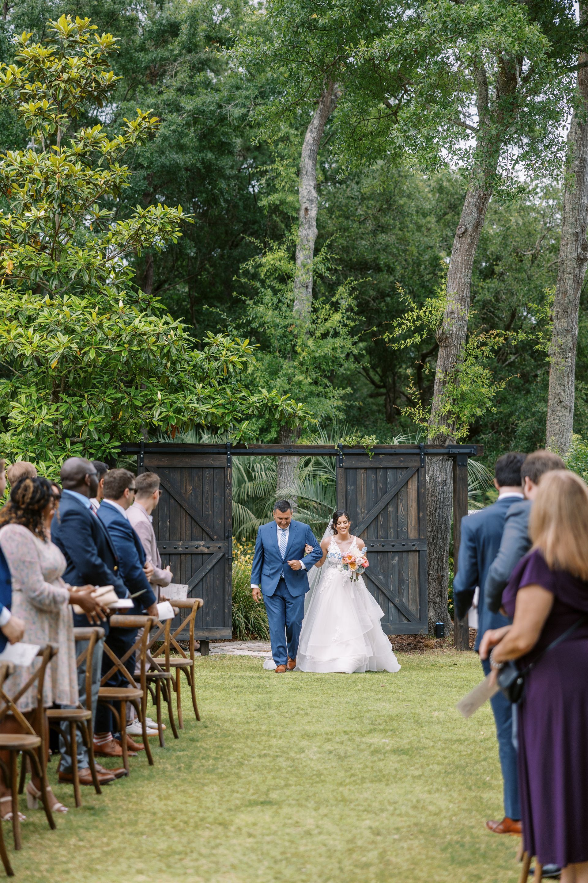Bride and groom walk down an outdoor aisle at a garden wedding as guests watch.