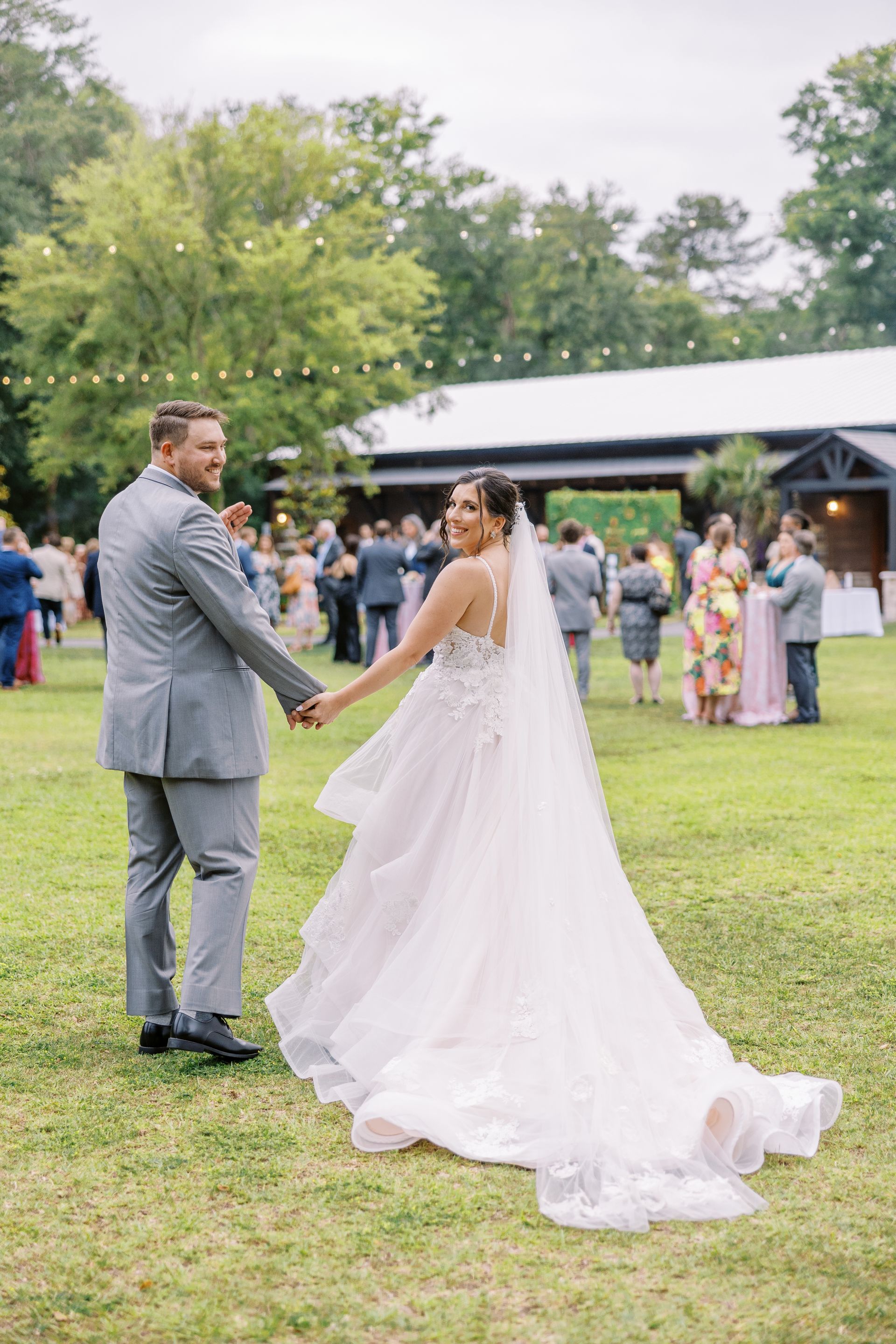 Bride and groom holding hands at an outdoor wedding reception on a grassy lawn