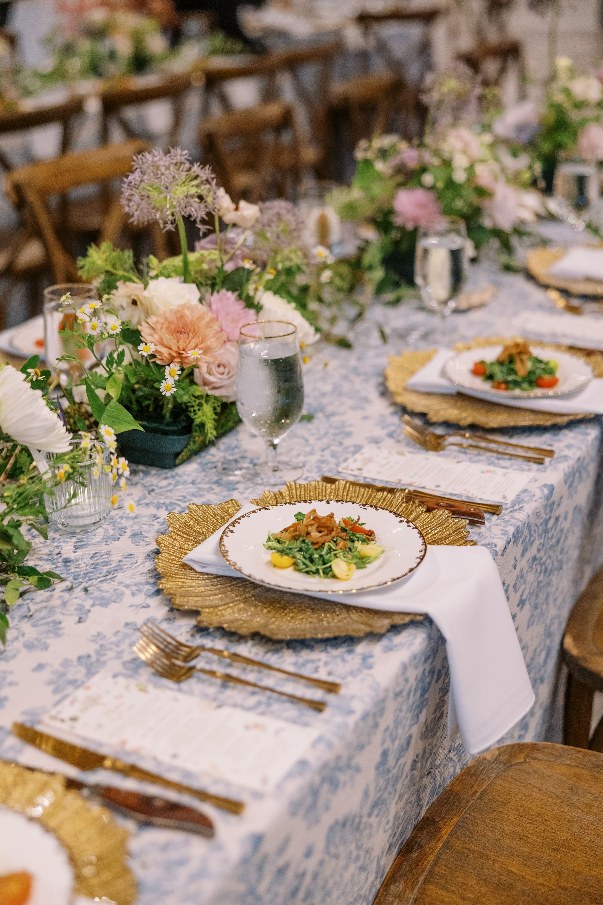 Elegant banquet table set with floral centerpieces, white plates, and gold flatware in a rustic dining room