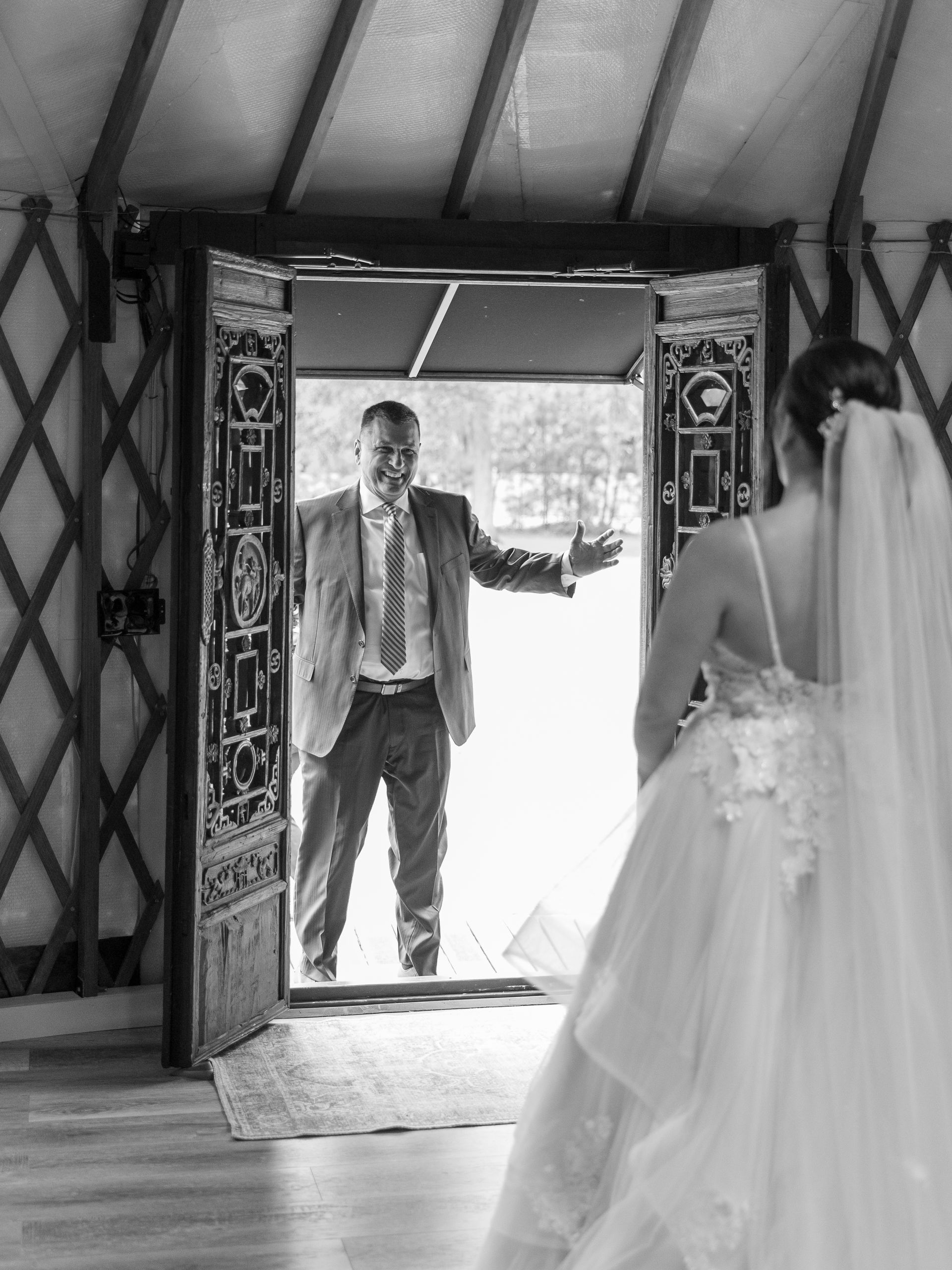 Bride facing a man in a doorway, with bright outdoors behind him and draped tent interior around them