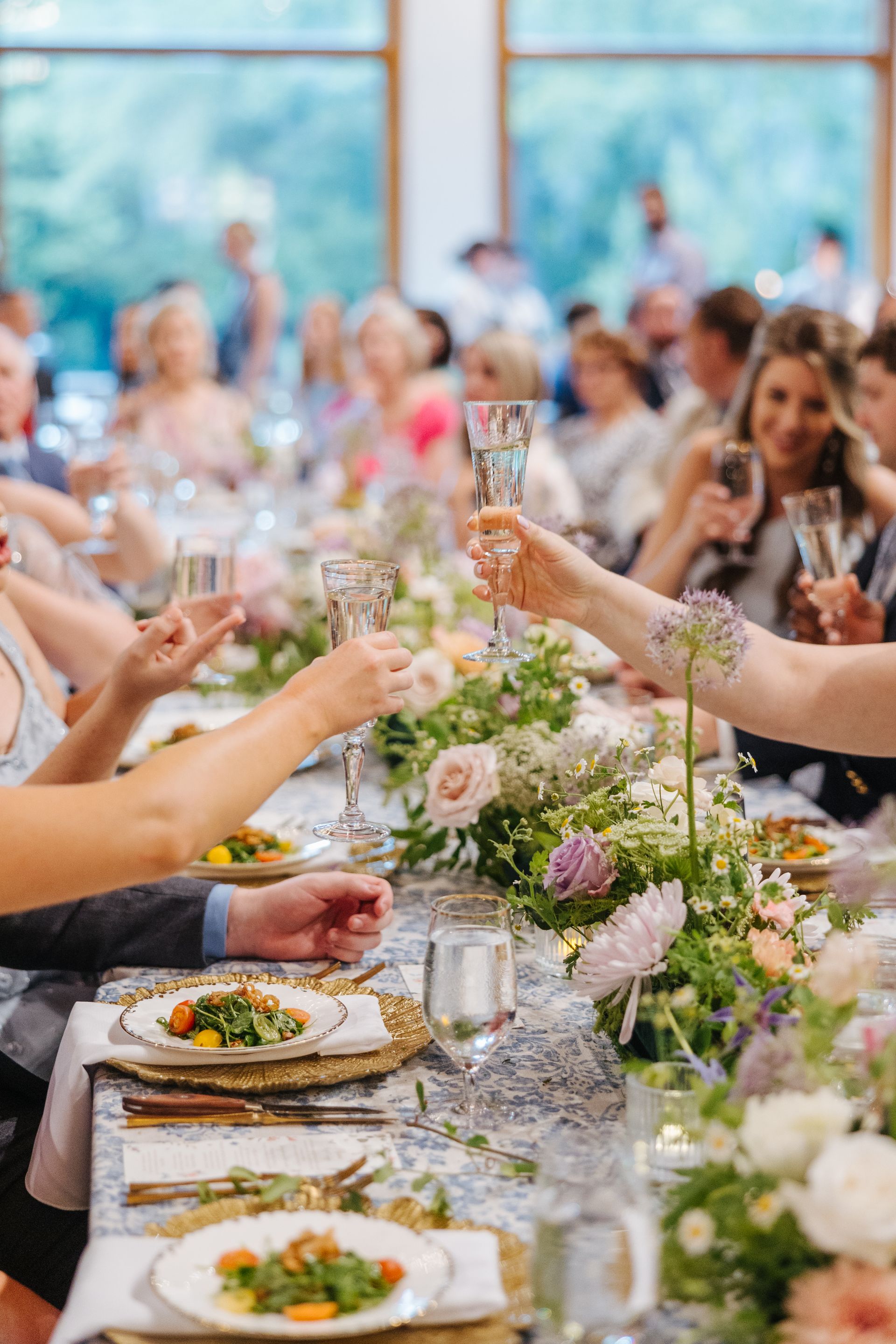 Guests toast at a floral banquet table during a bright indoor celebration.