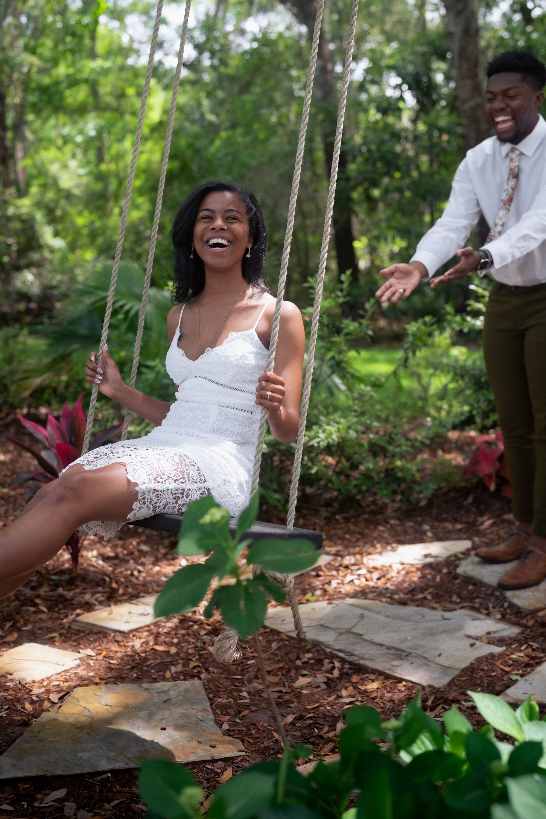 Couple on swings in a lush garden, smiling and reaching toward each other.