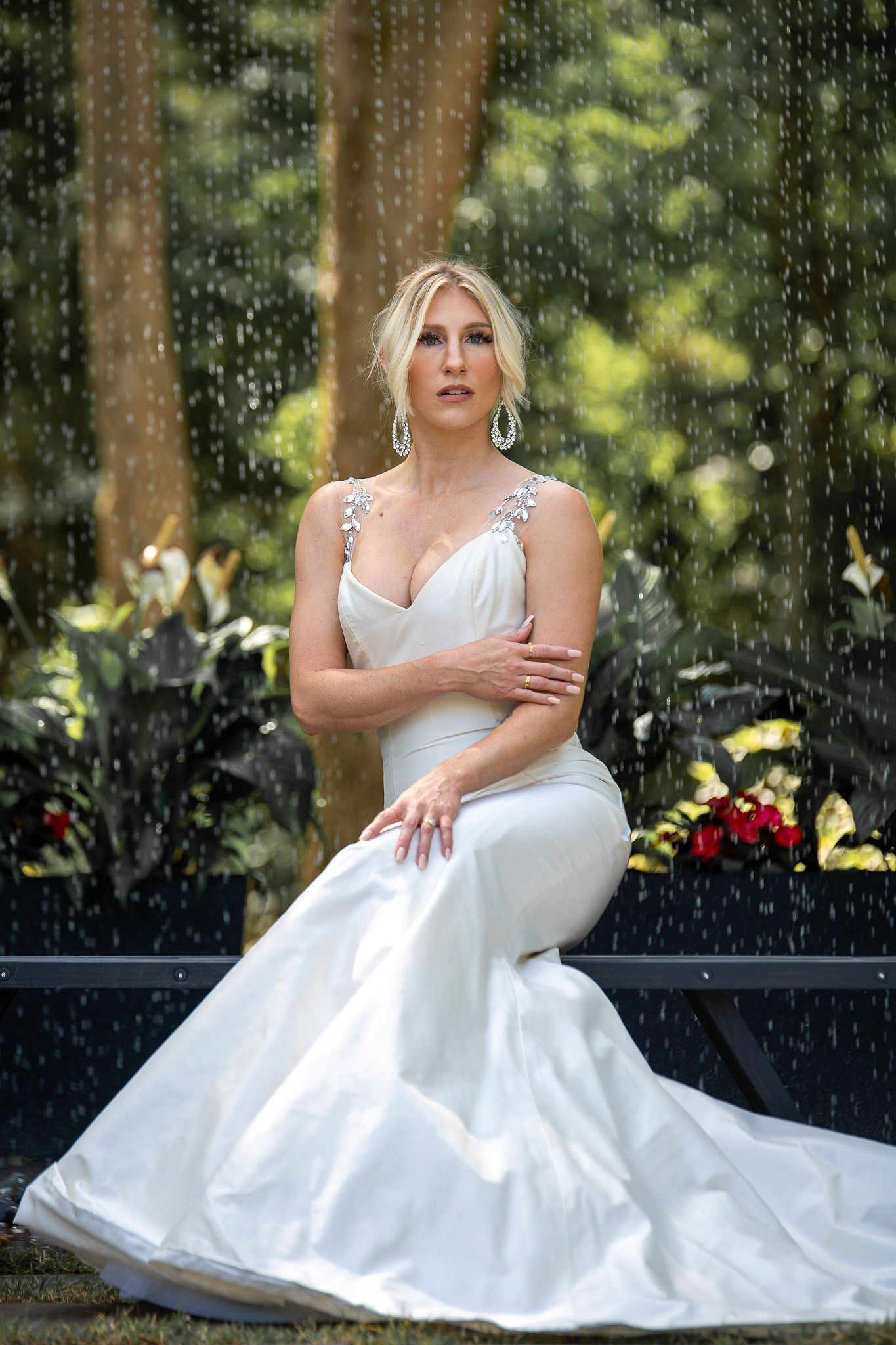 Woman in a white gown seated by a rain-streaked window in a garden setting