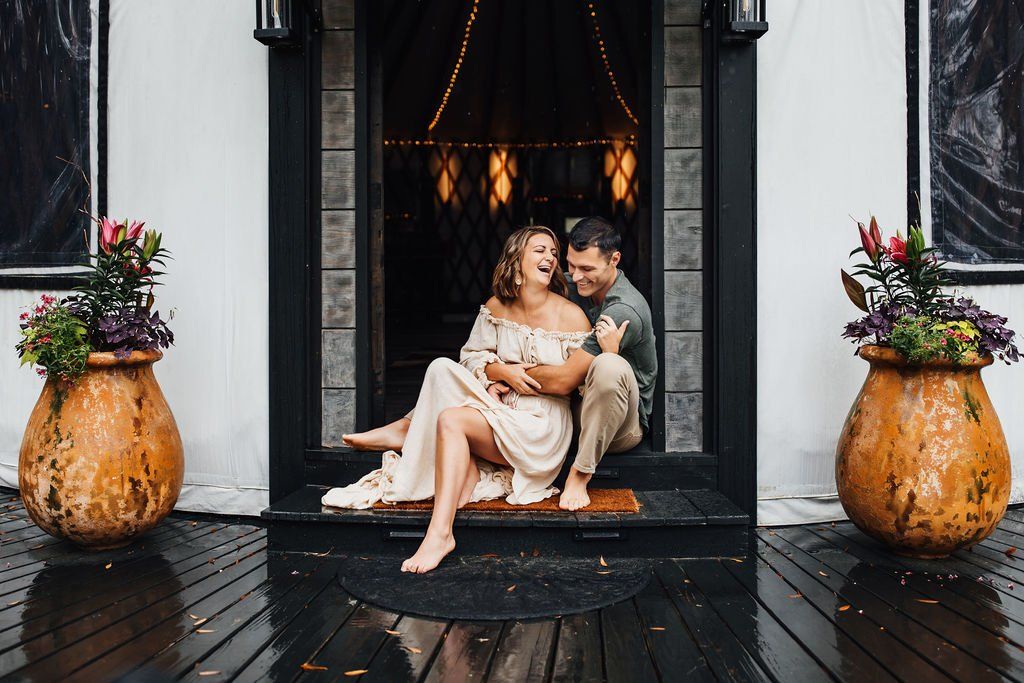 Couple seated on a doorway step with a baby, framed by floral pots and dark wood accents