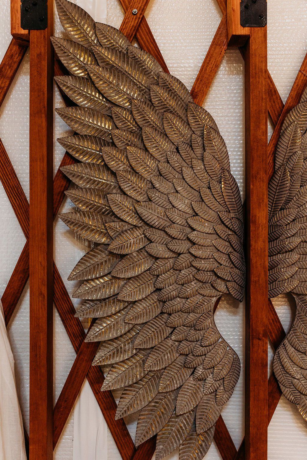 Decorative metal wing sculpture with layered bronze feathers on a wooden lattice