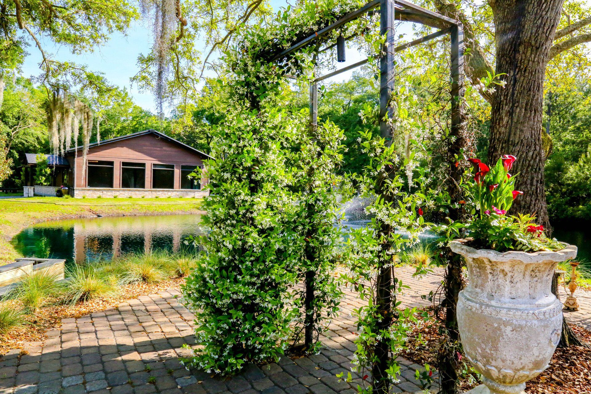 Garden path beside a reflecting pond, with a small pavilion and lush greenery in bright sunlight
