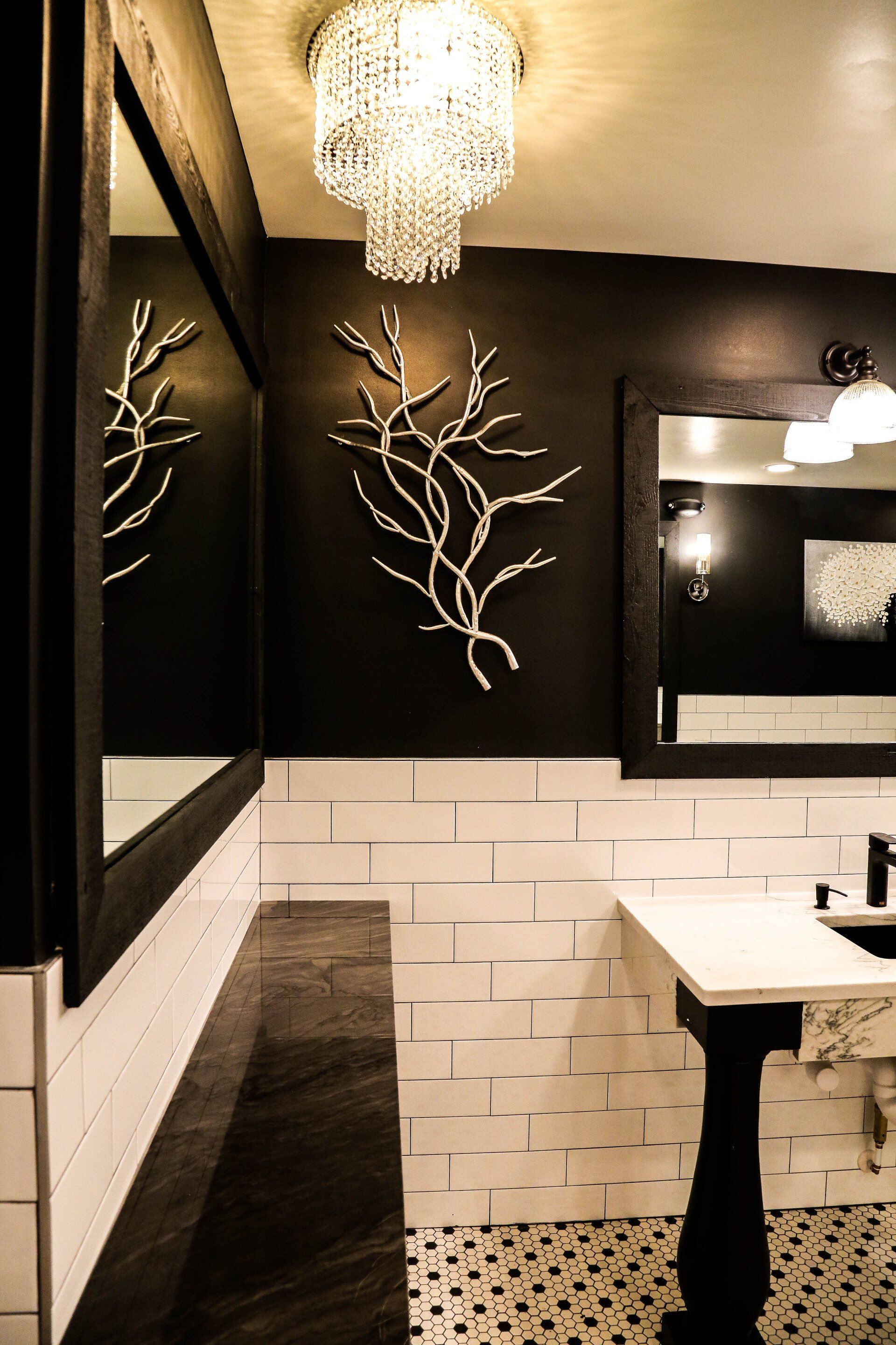 Modern bathroom with black-and-white tile, chandelier, mirror, and decorative branch wall art