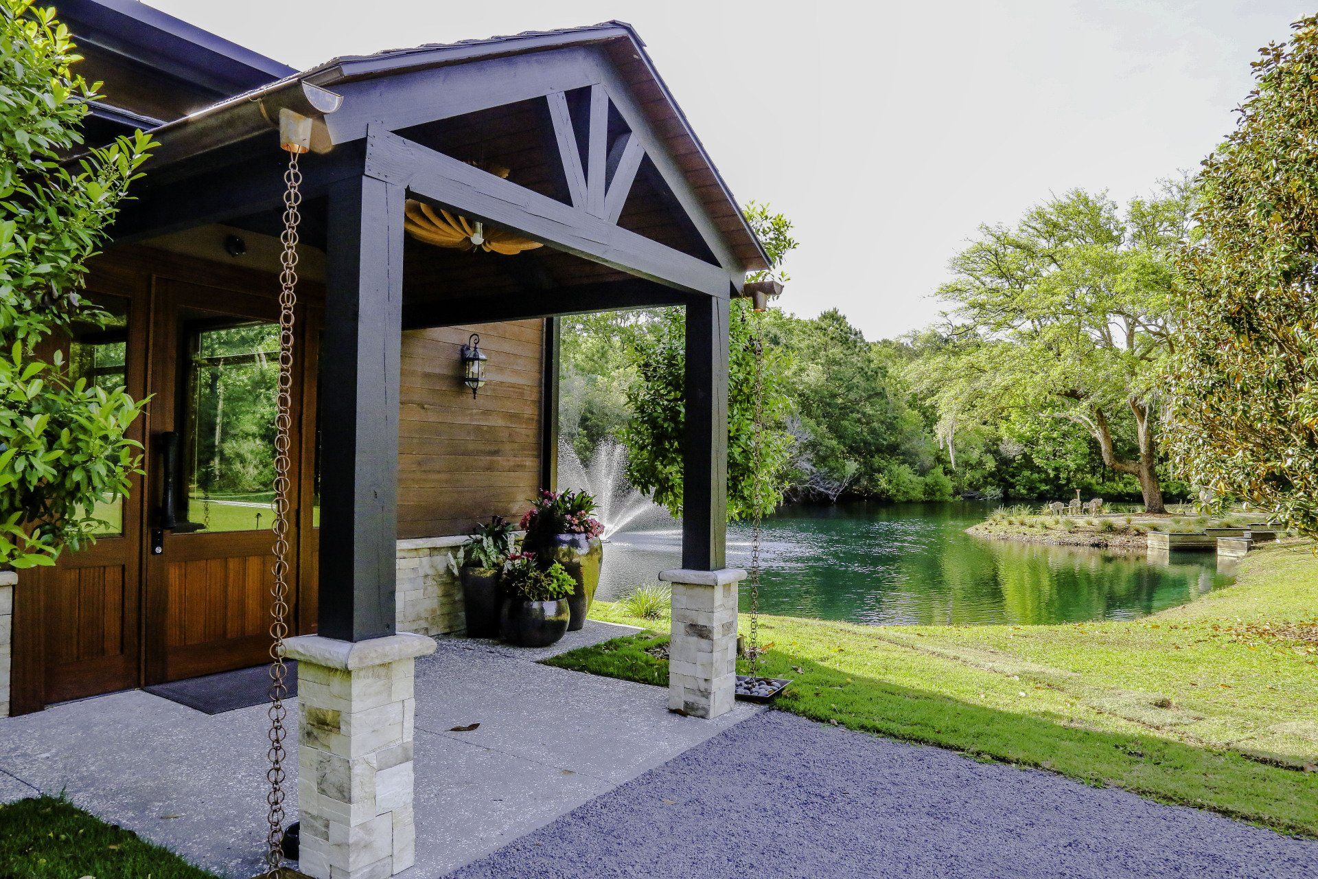 Wooden cabin porch overlooking a calm pond and green lawn on a sunny day