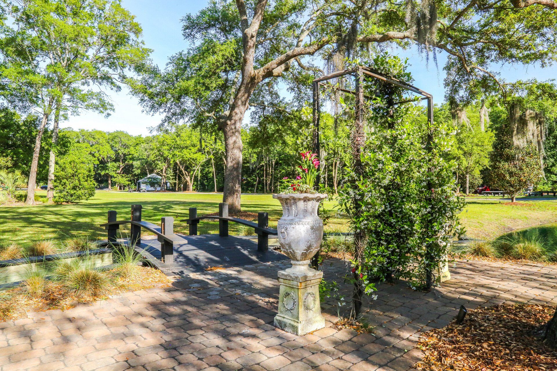 Sunlit park path with a small bridge, fountain, and trees beside a pond