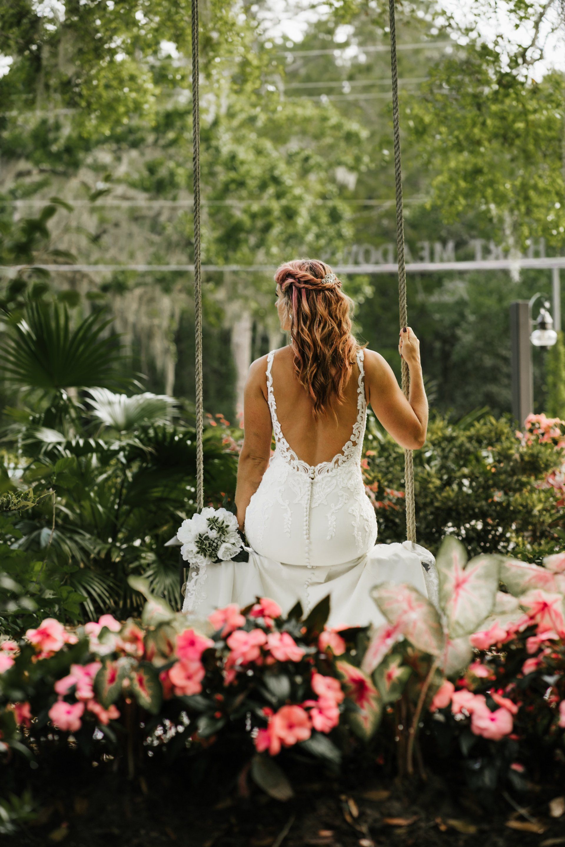 Bride in a white dress standing among pink flowers in a lush garden ceremony setting