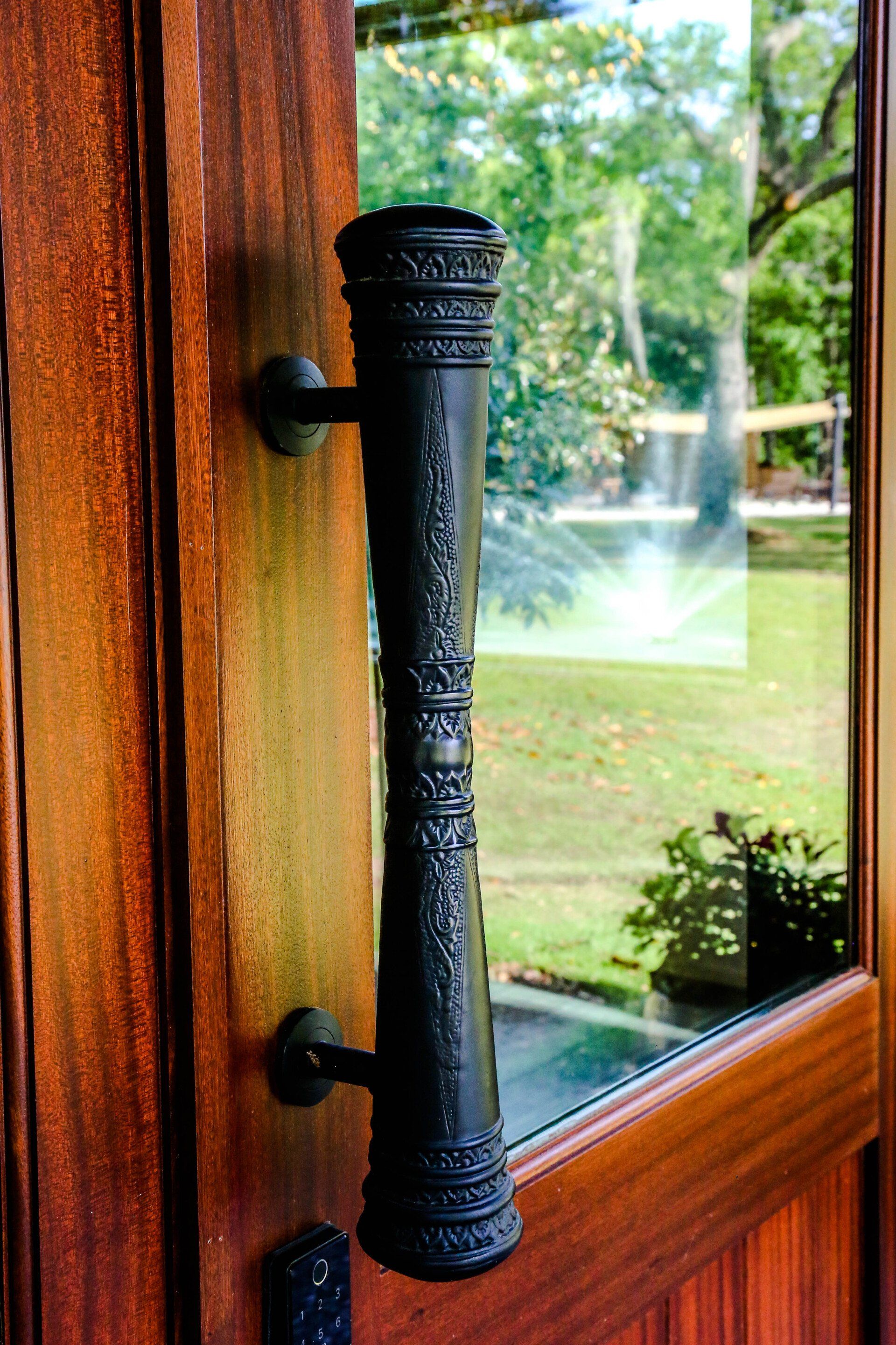 Black door handle on a wooden-framed glass door with a garden visible outside
