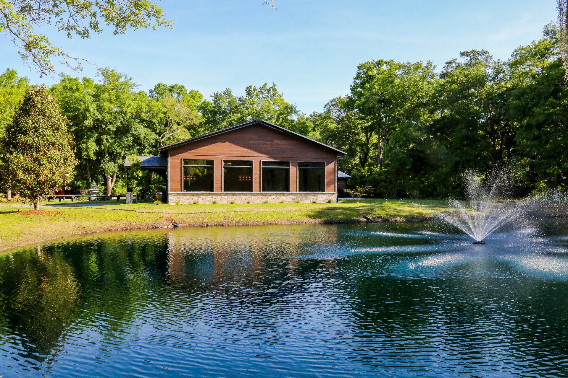 Pond with fountain spray in front of a brick building surrounded by green trees