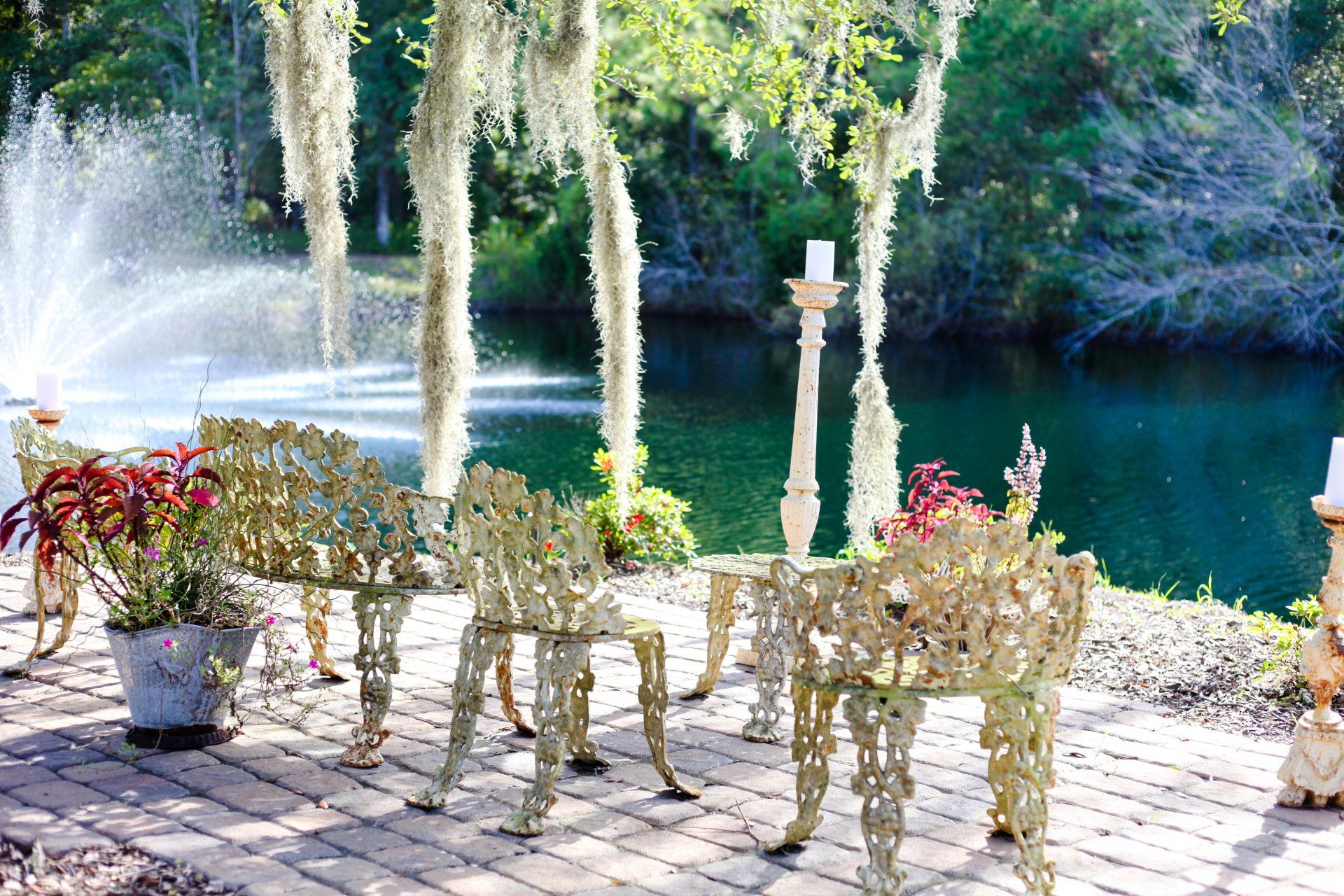 Outdoor patio with gold wire chairs and table beside a fountain and green lake surrounded by trees