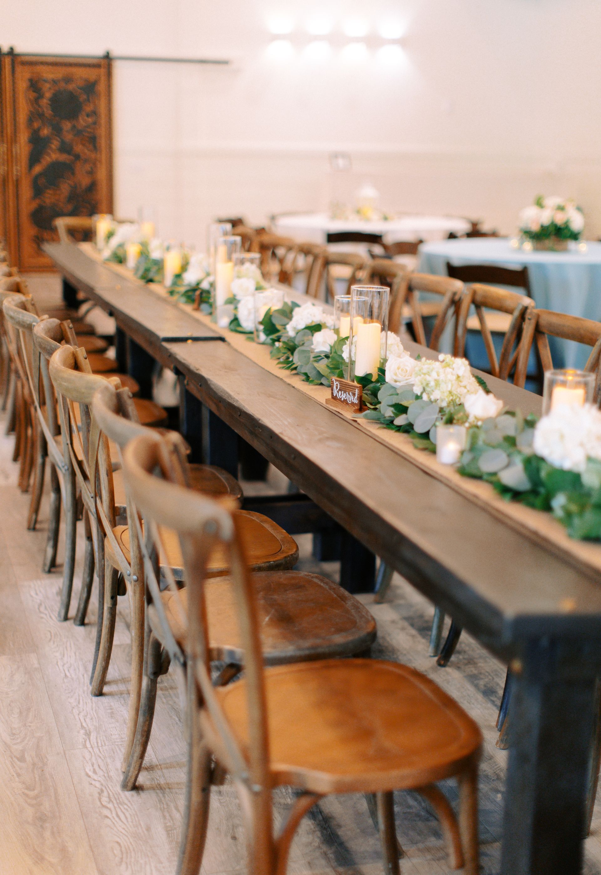 Long banquet tables with wooden chairs and floral centerpieces in a bright dining room
