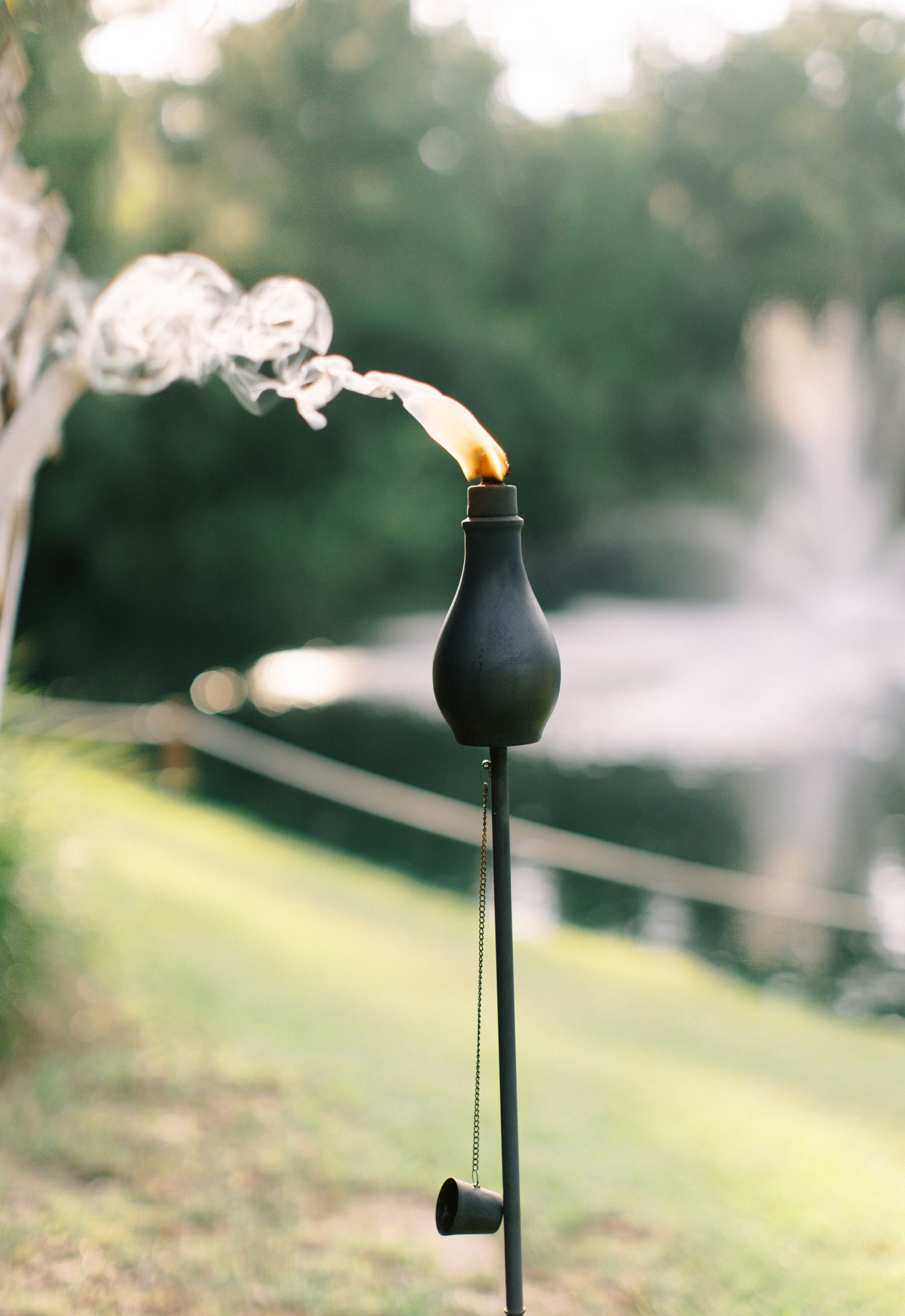 Black outdoor torch with a small flame and smoke in a grassy garden setting