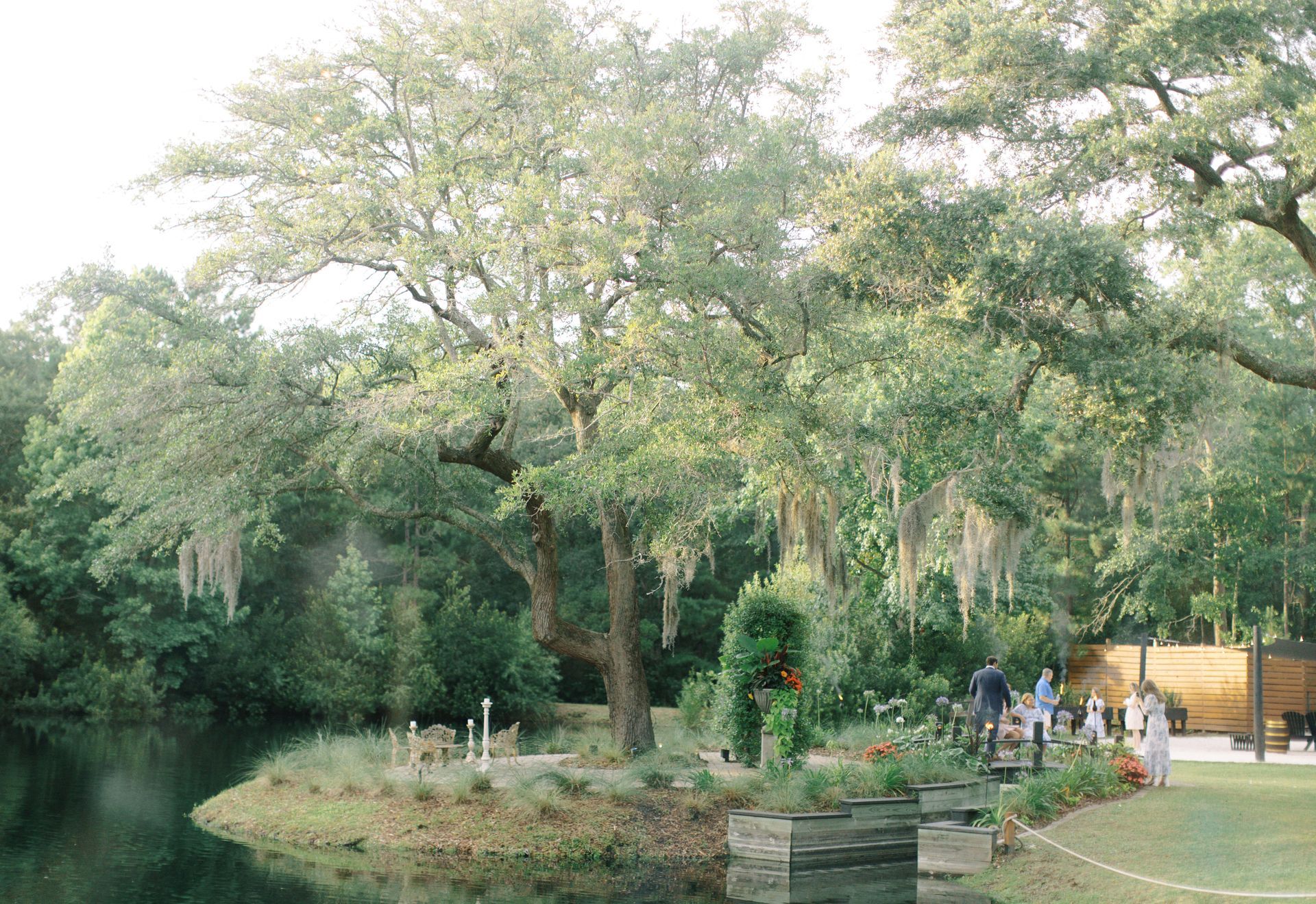 Wooded park with a small pond, lush trees, and people near a path and yellow kiosk