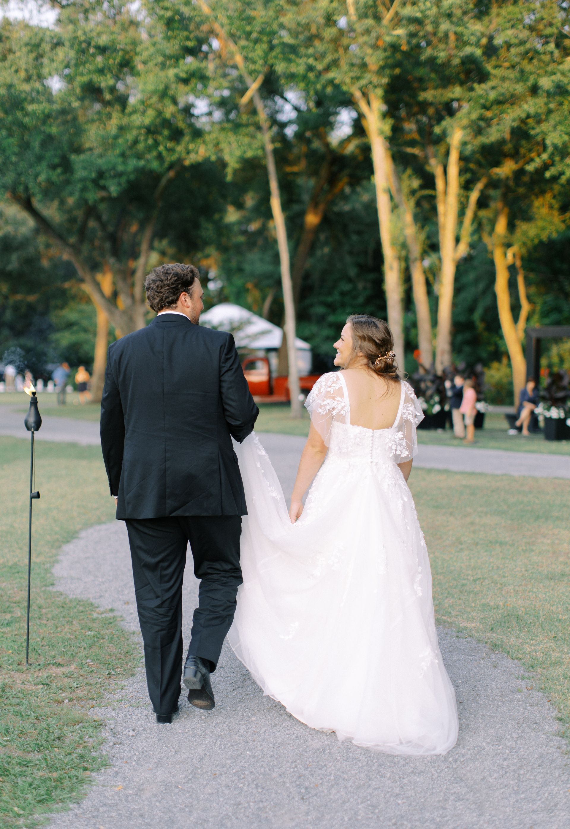 Bride and groom walking hand in hand along a park path at an outdoor wedding ceremony