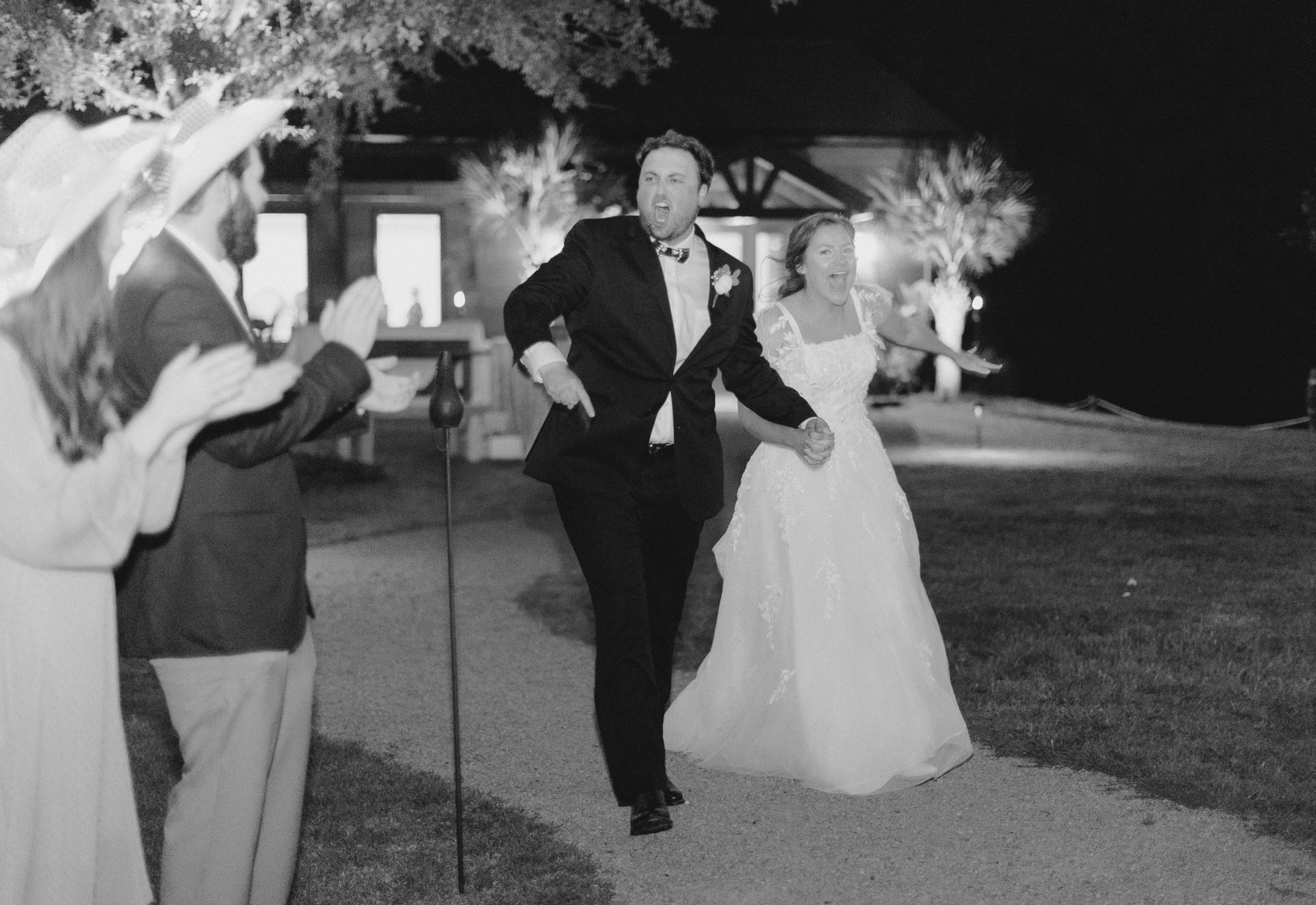Bride and groom walk down an outdoor path at night during a wedding celebration.