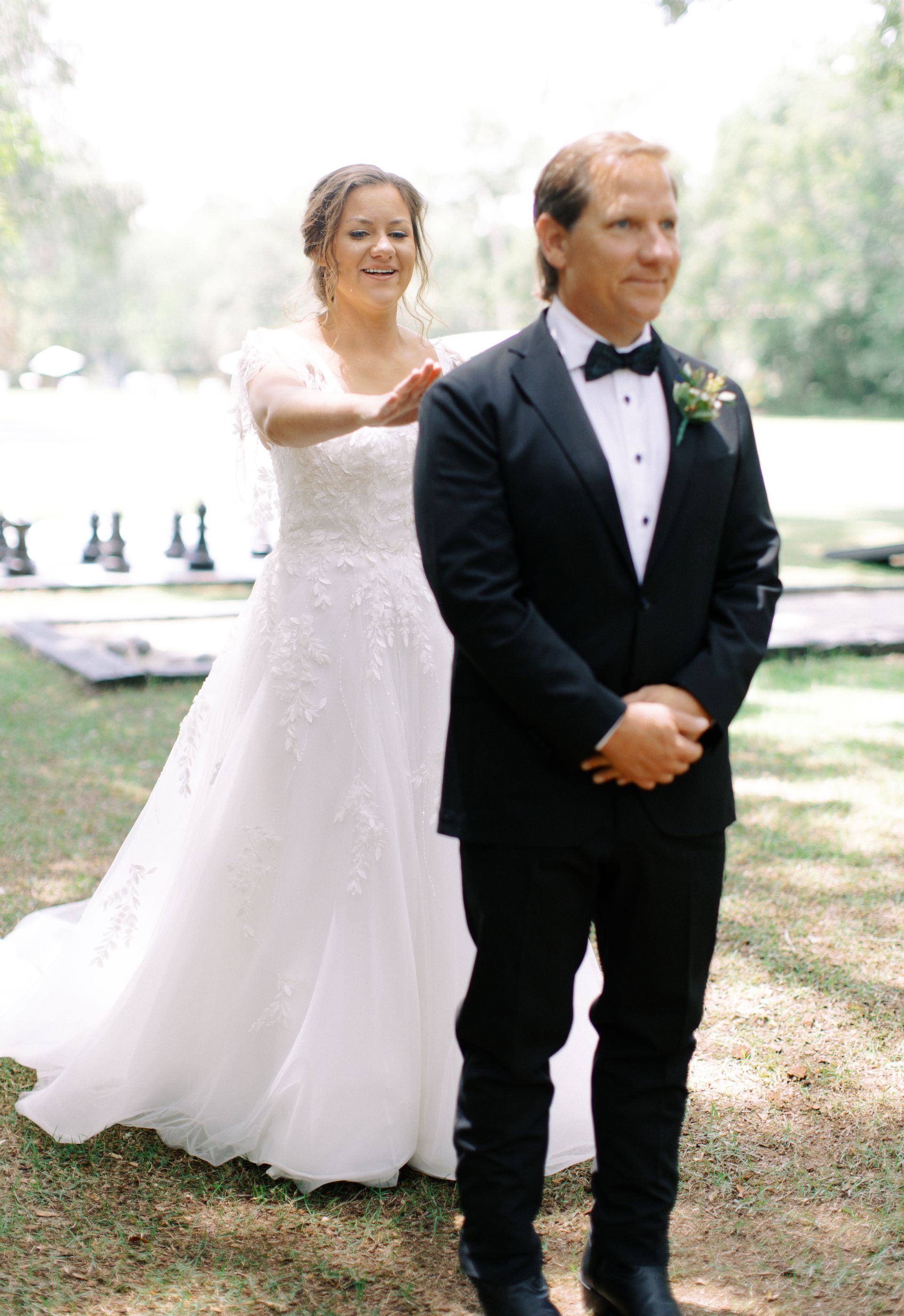 Bride adjusting groom’s tuxedo outdoors by a lakeside in a wedding ceremony