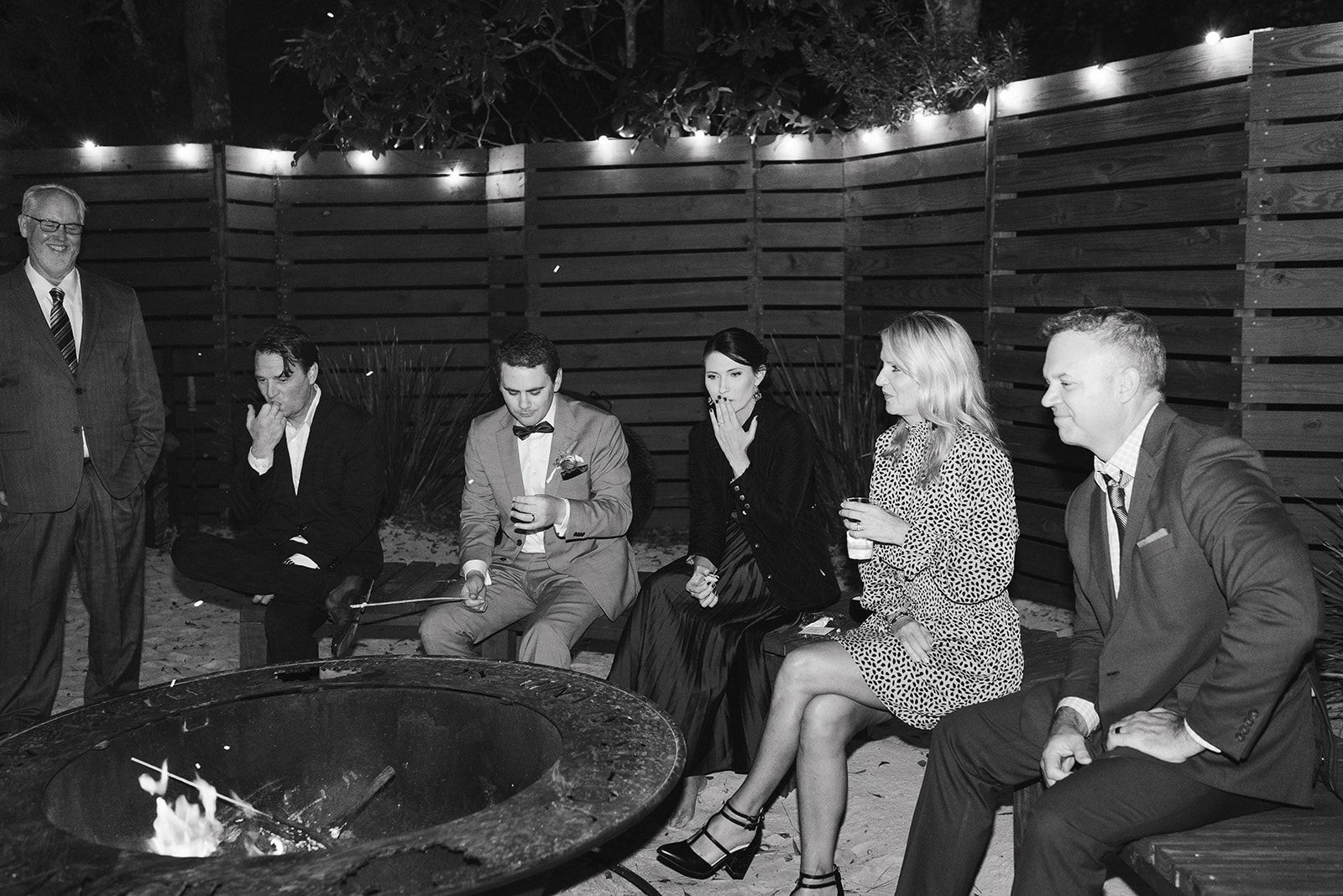 People seated around a fire pit in a dim outdoor lounge at night