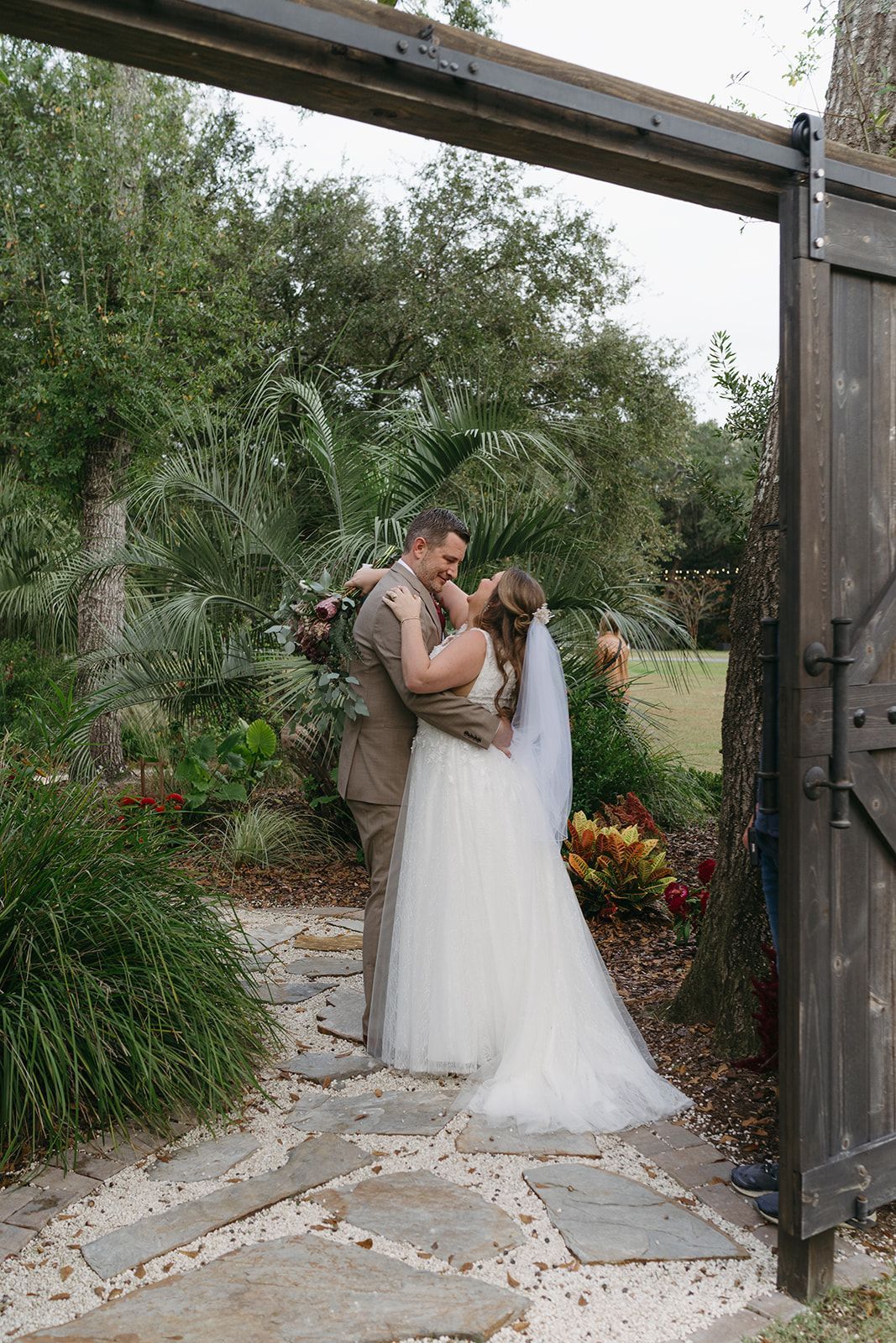 Bride and groom embrace in a garden doorway surrounded by flowers and greenery