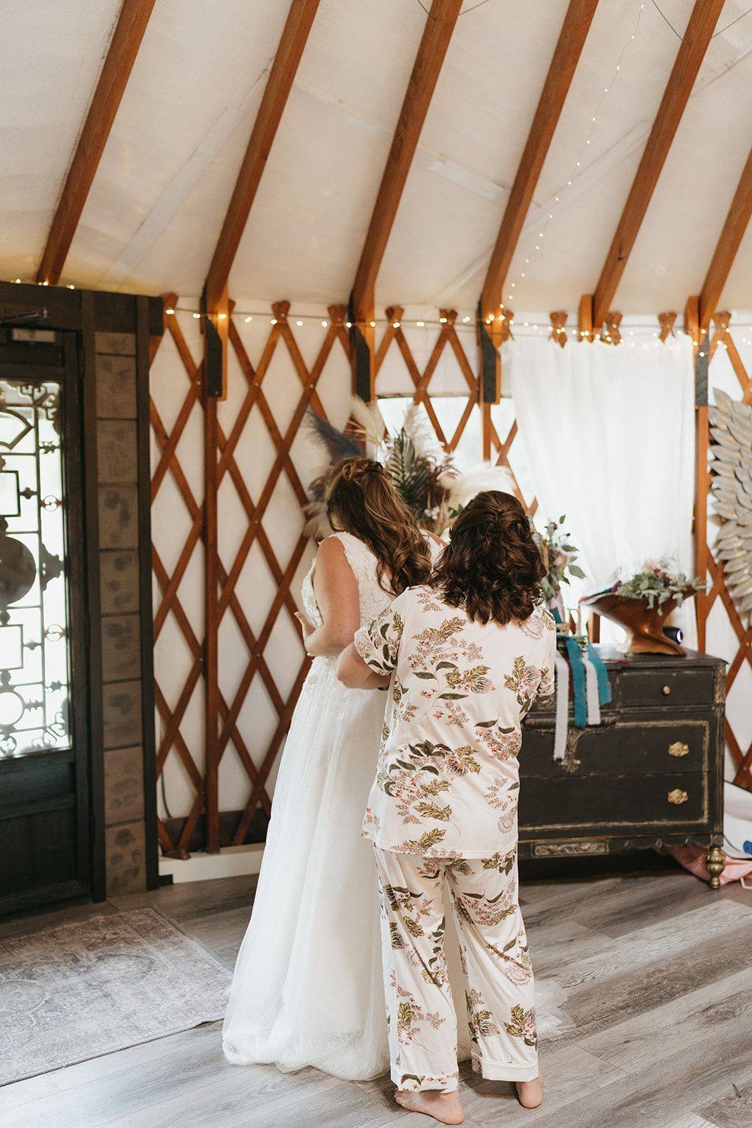 Bride and companion embracing in a rustic yurt-like wedding venue with wood lattice walls and soft white drapery