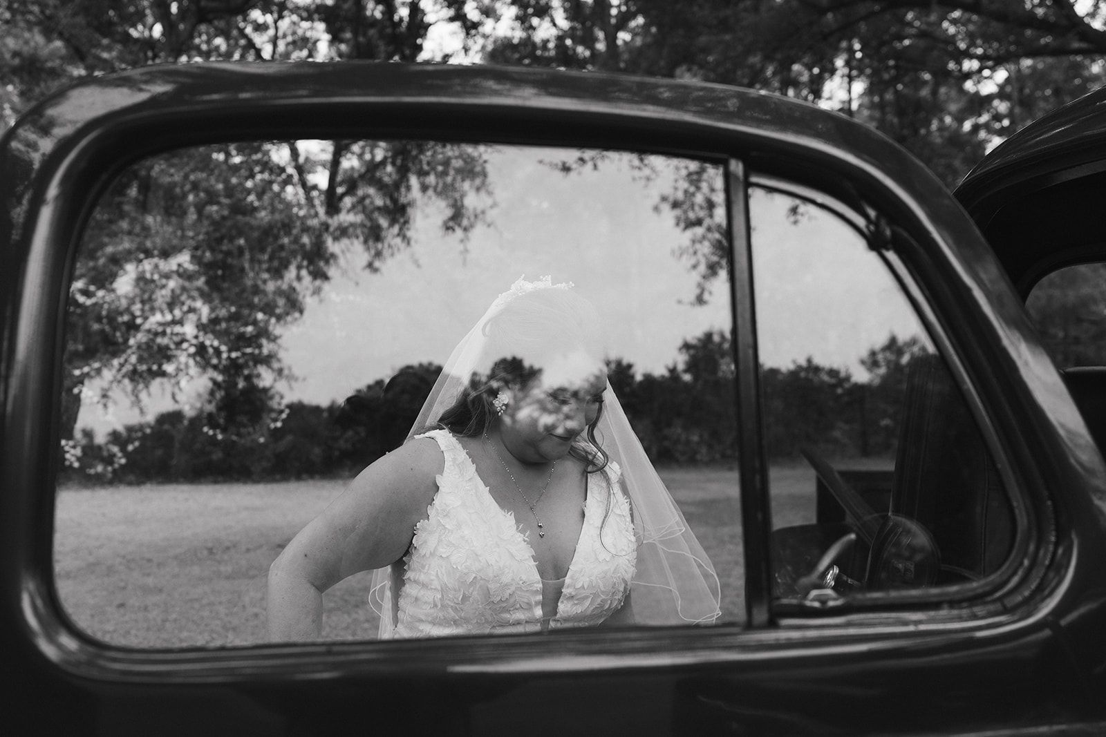Person in a white dress seen through a car window, standing outdoors by a field.
