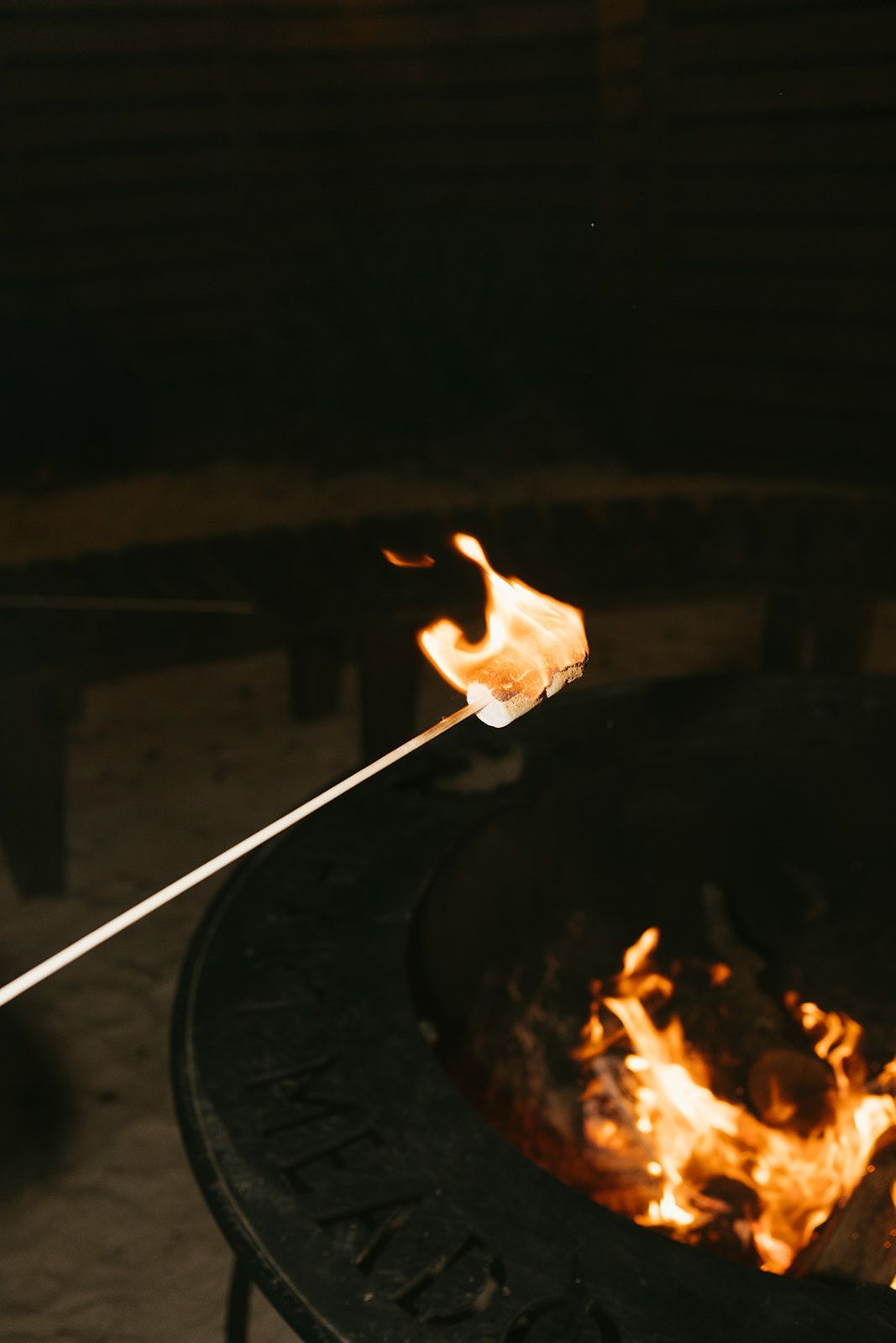 Hand holding a lit marshmallow over a fire pit at night