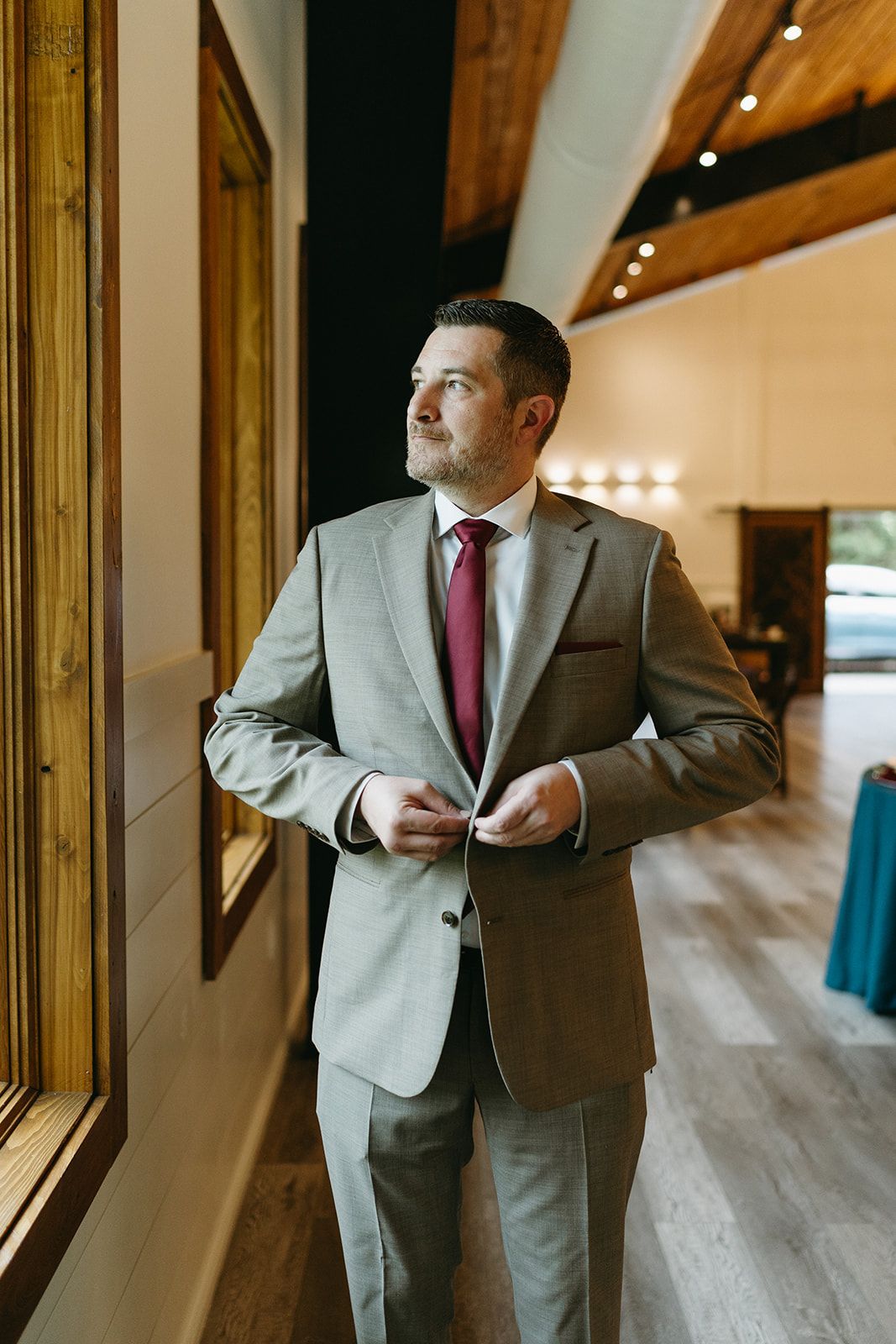 Man adjusting his gray suit jacket in a warmly lit hallway with wood floors and framed wall art