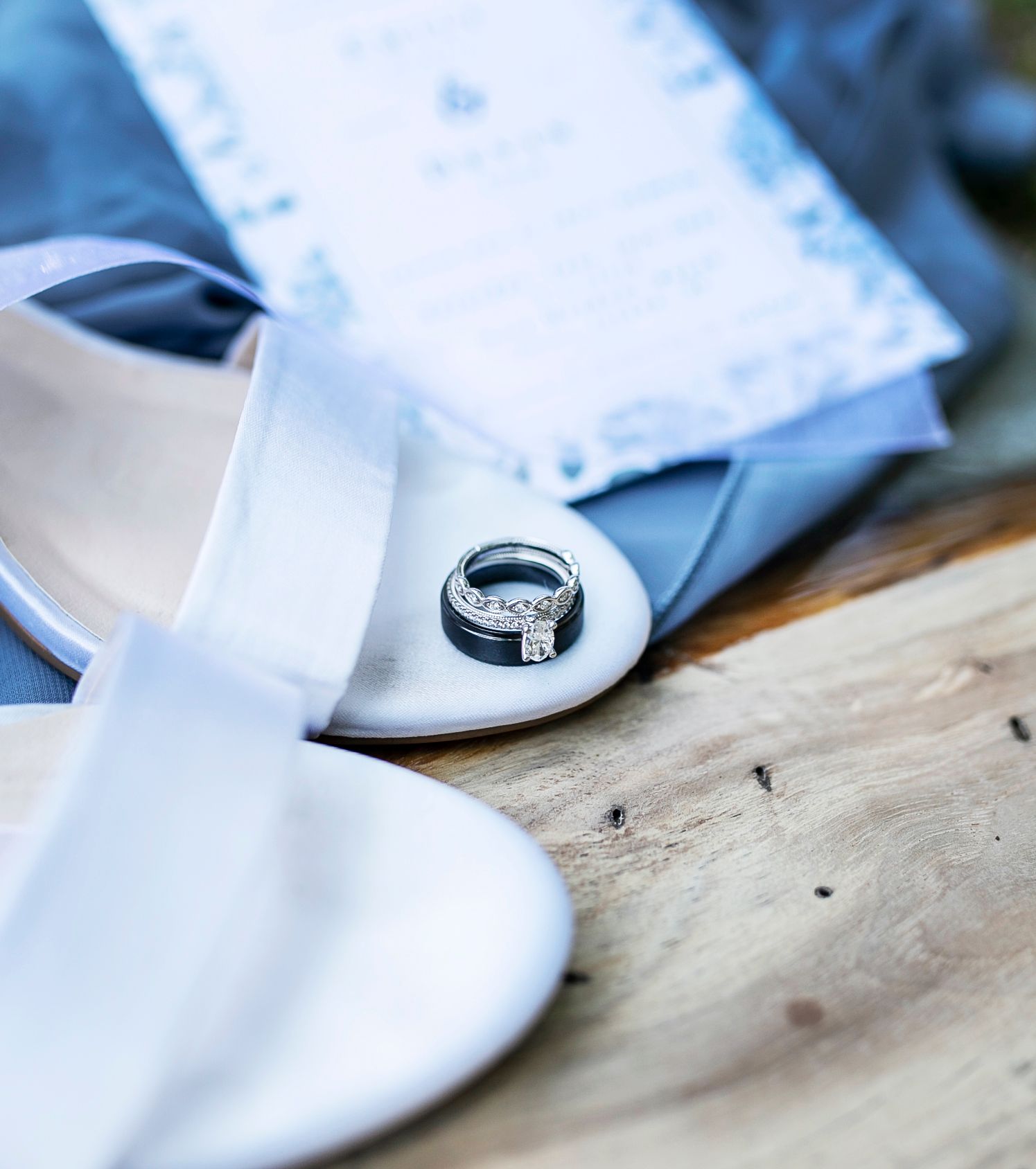 Ring on white bridal shoes beside a blue suit on a wooden surface