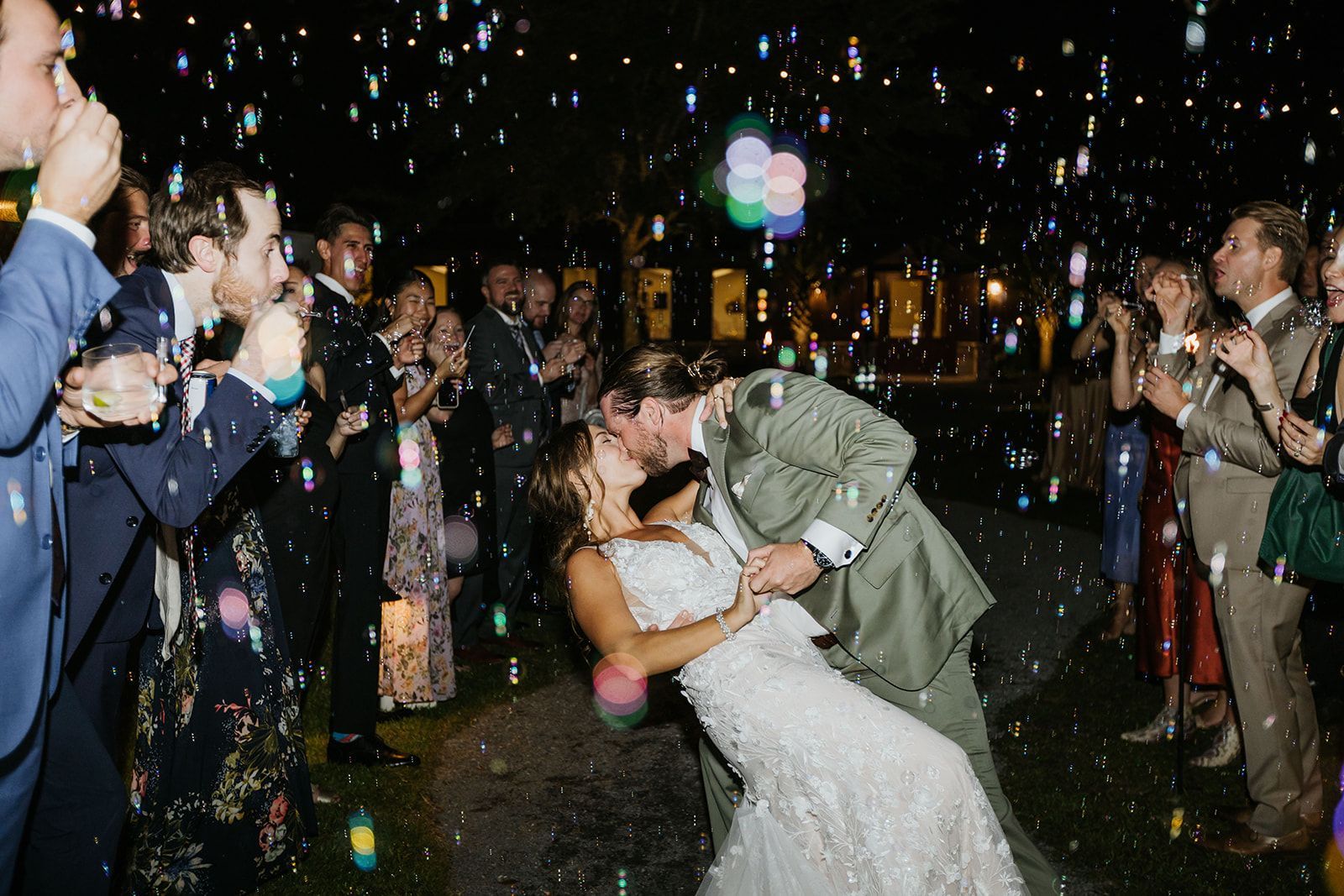 Wedding couple kissing outdoors under confetti and sparklers, guests cheering nearby