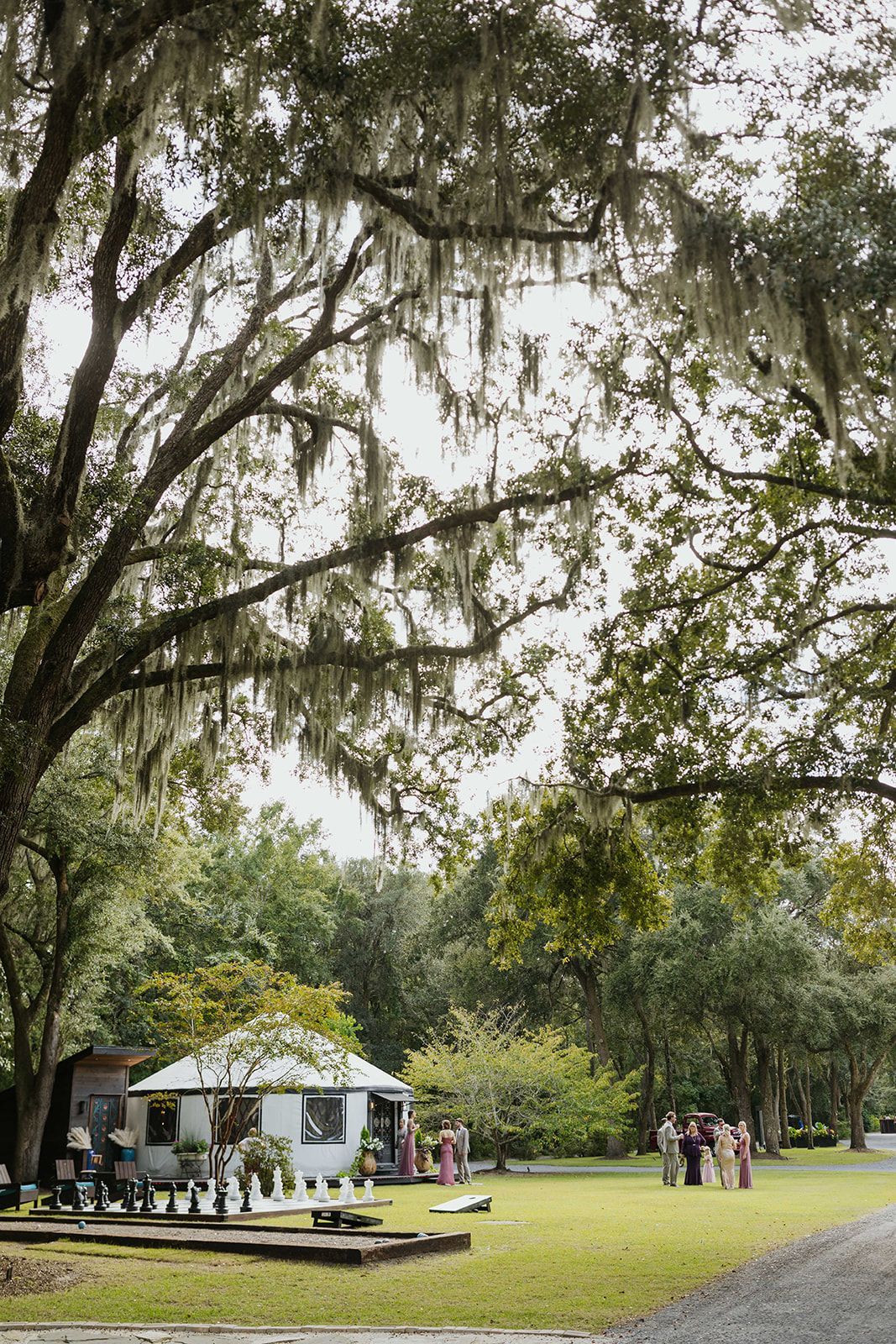 People gathered near a white pavilion in a grassy park under large trees