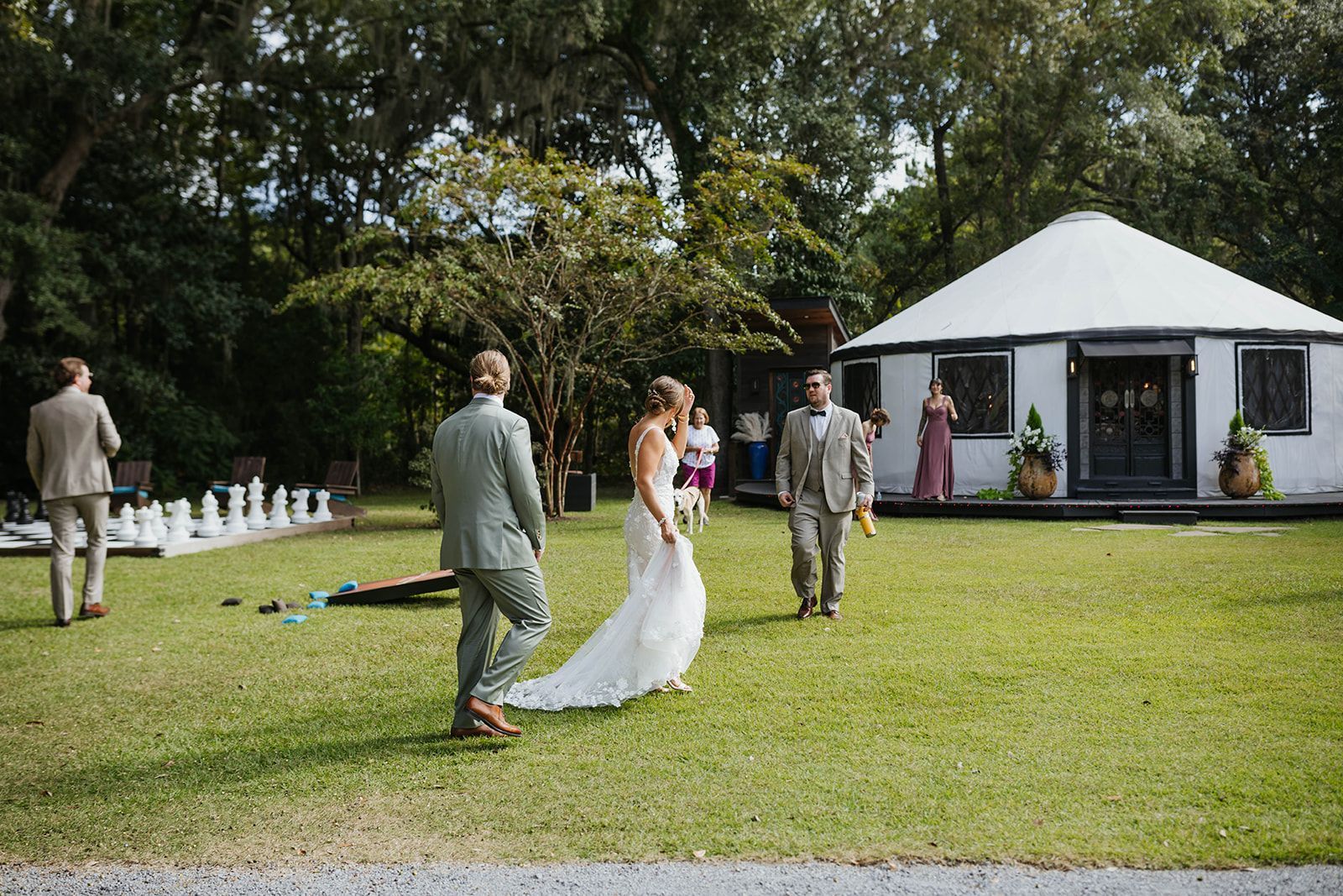 Wedding guests on a lawn near a white tent, with the bride in a long white dress walking away.