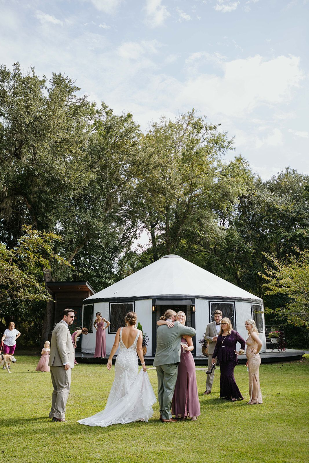 People mingling at an outdoor garden wedding under a white tent, with trees and grass around them.