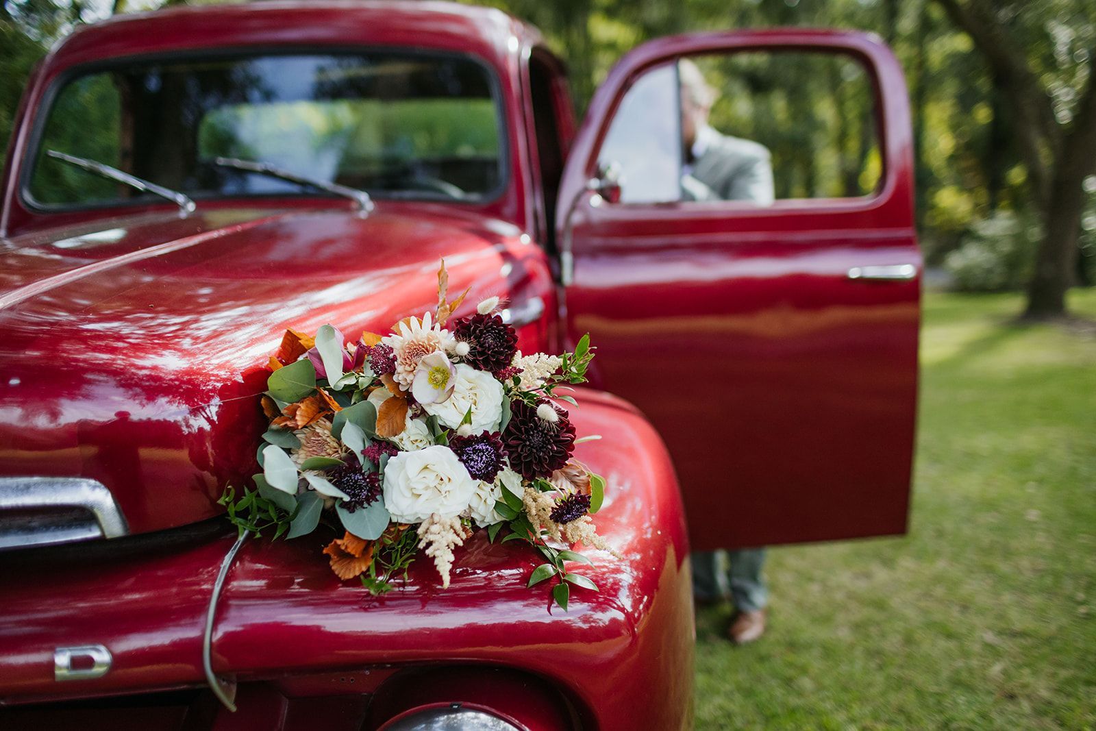 Red vintage truck with a bouquet on the hood and an open door in a park