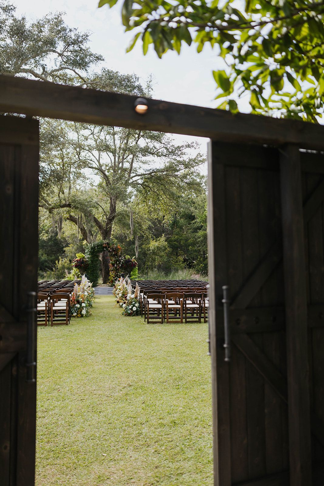 Open wooden gate framing a grassy outdoor venue with rows of chairs beneath trees