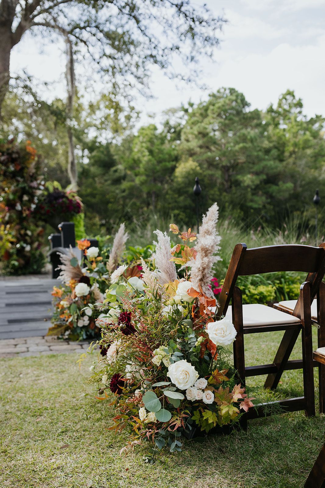 Flower arrangements beside wooden chairs on a grassy outdoor event lawn