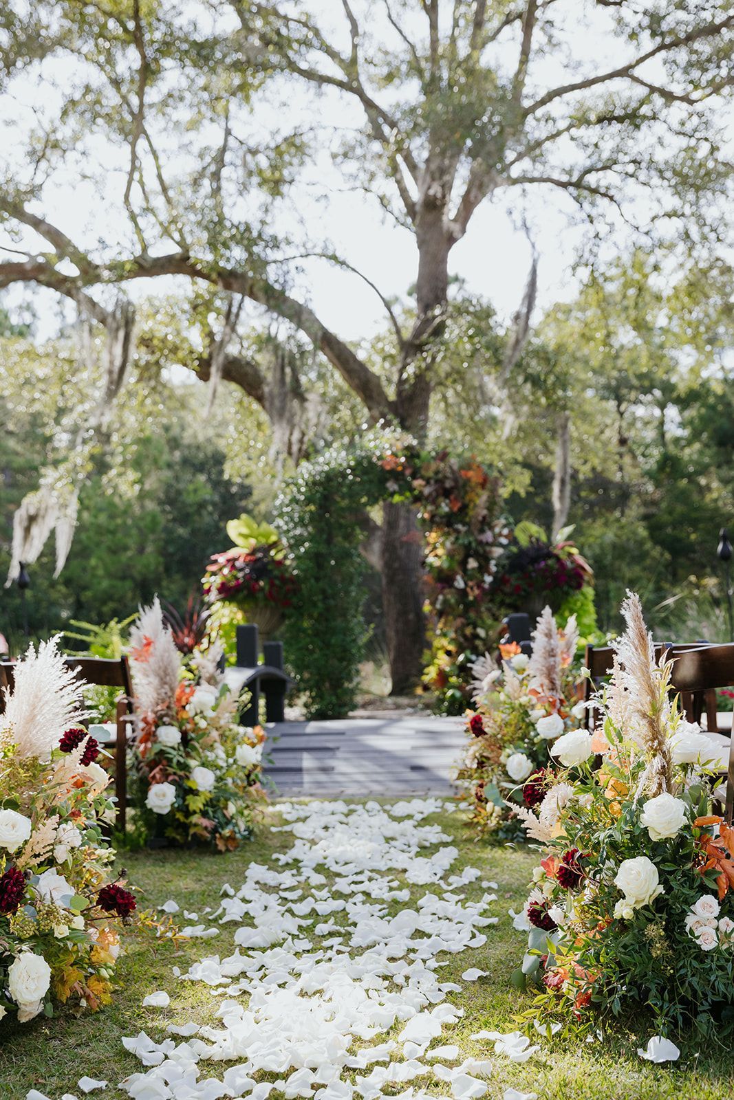 Flower-lined garden aisle with white petals, floral arch, and tall trees overhead