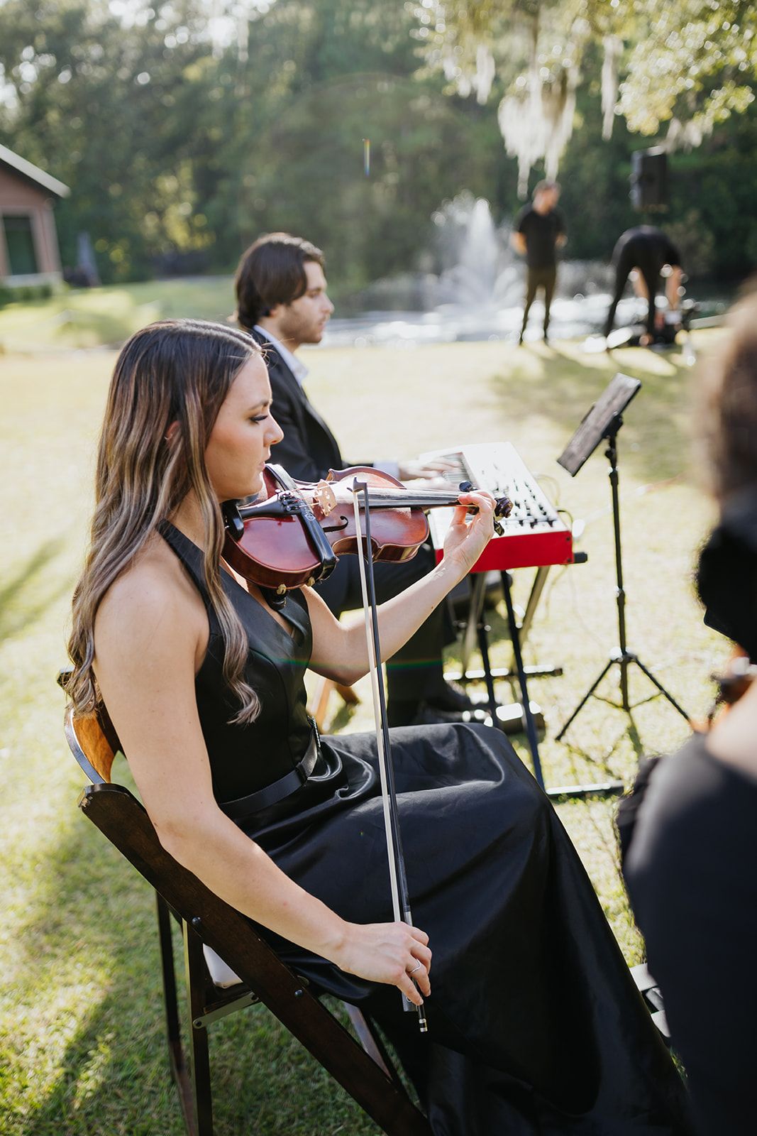 Violinist in a black dress plays outdoors at a small garden performance with a music stand nearby